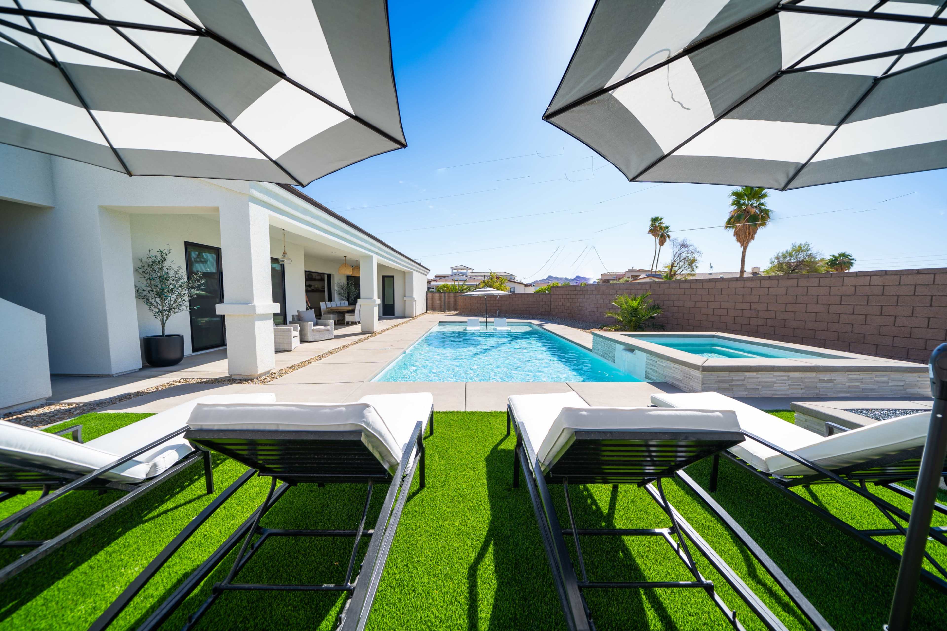The scene shows a backyard with two lounge chairs facing a swimming pool, surrounded by palm trees and a covered patio.