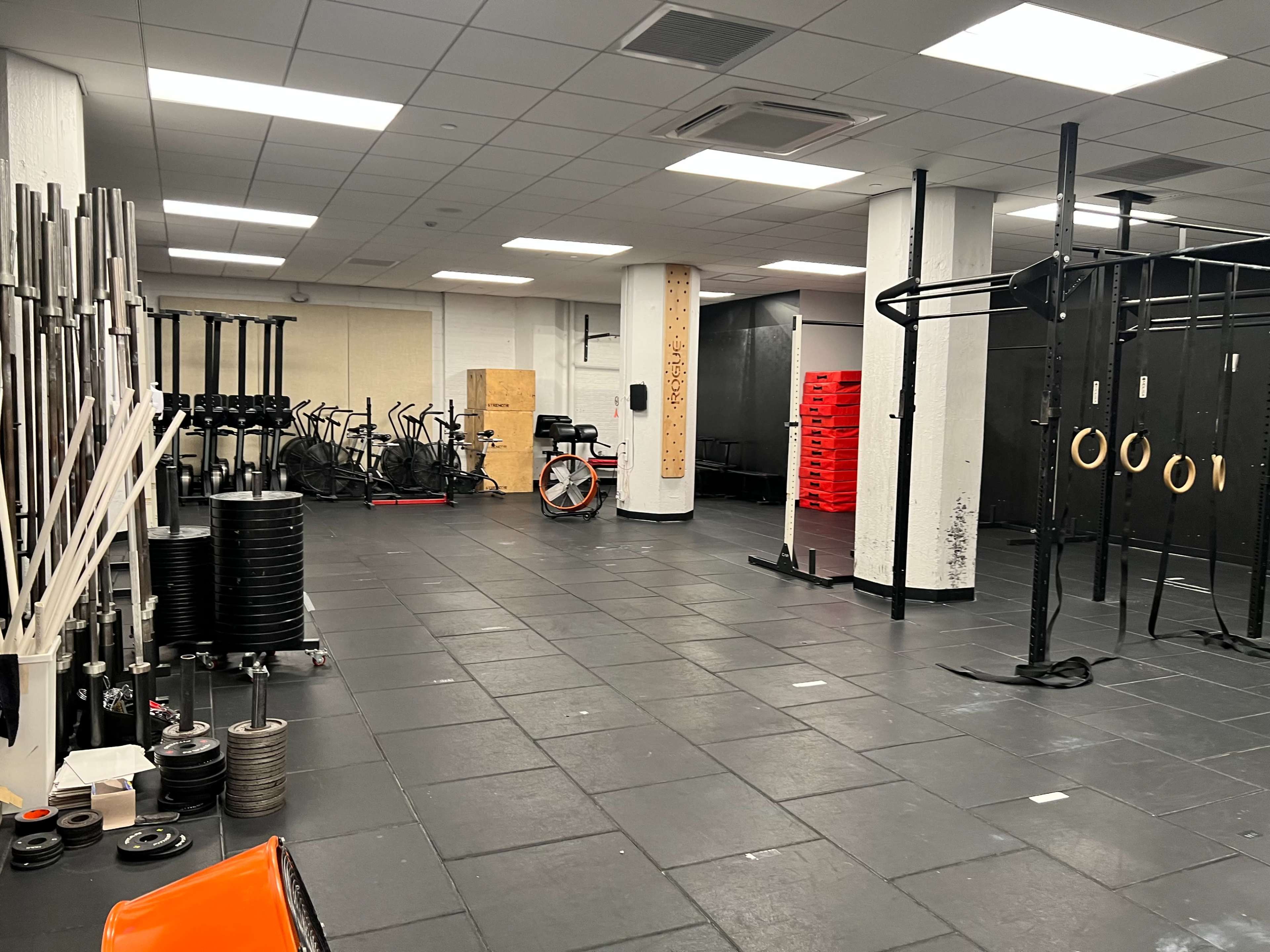 A spacious gym with exercise equipment, including weights, stationary bikes, and a pull-up station, arranged in a clean and well-lit environment.