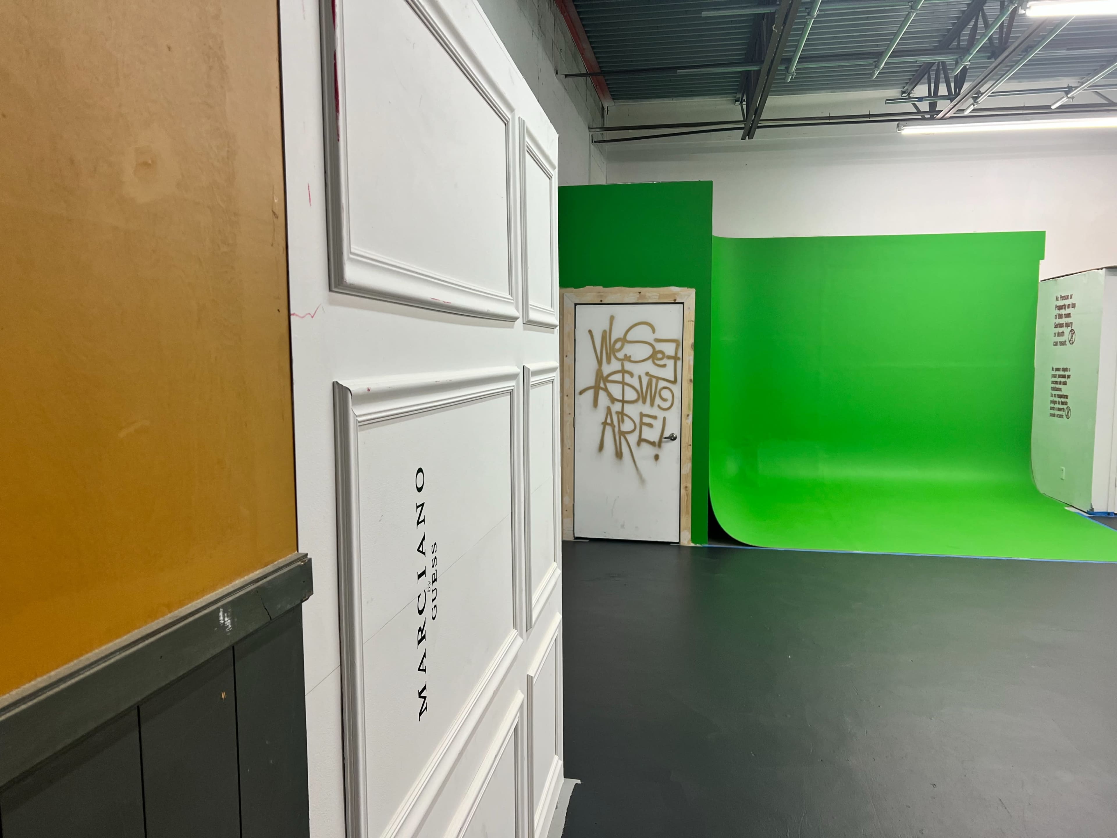 A studio with a white wall featuring the name "Marciano," a door with graffiti, and a green screen backdrop in the background.