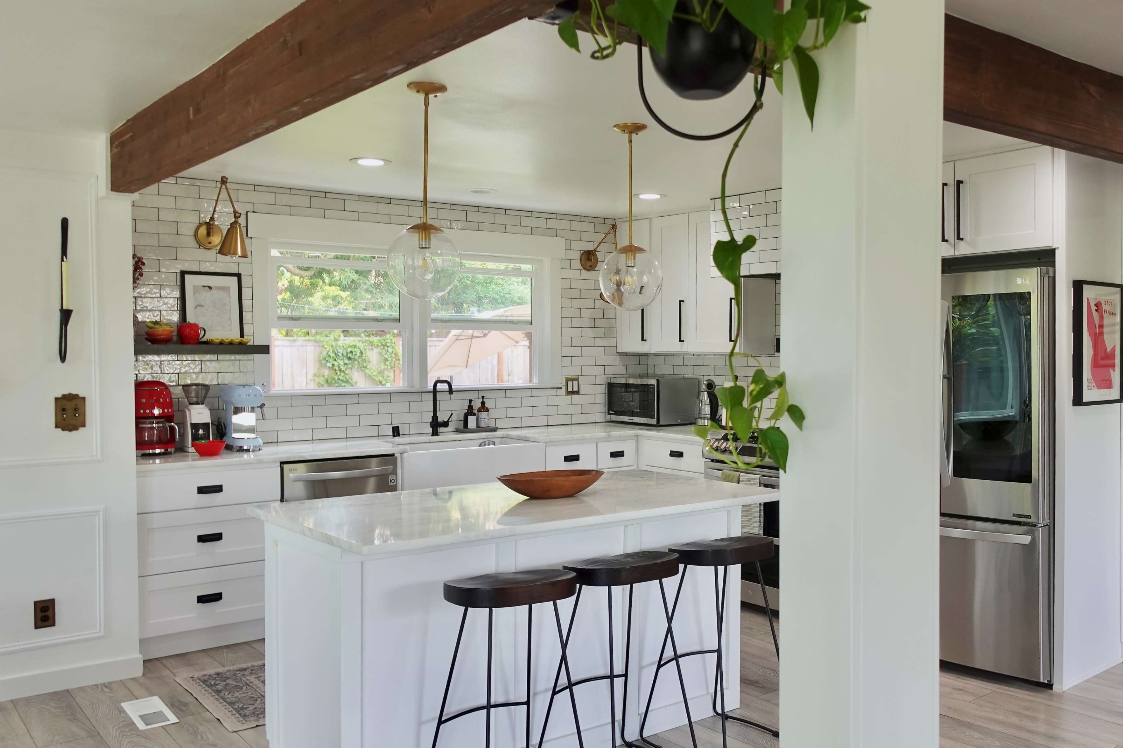 A modern kitchen features white cabinetry, a central island with bar stools, and a mix of stainless steel and black appliances.