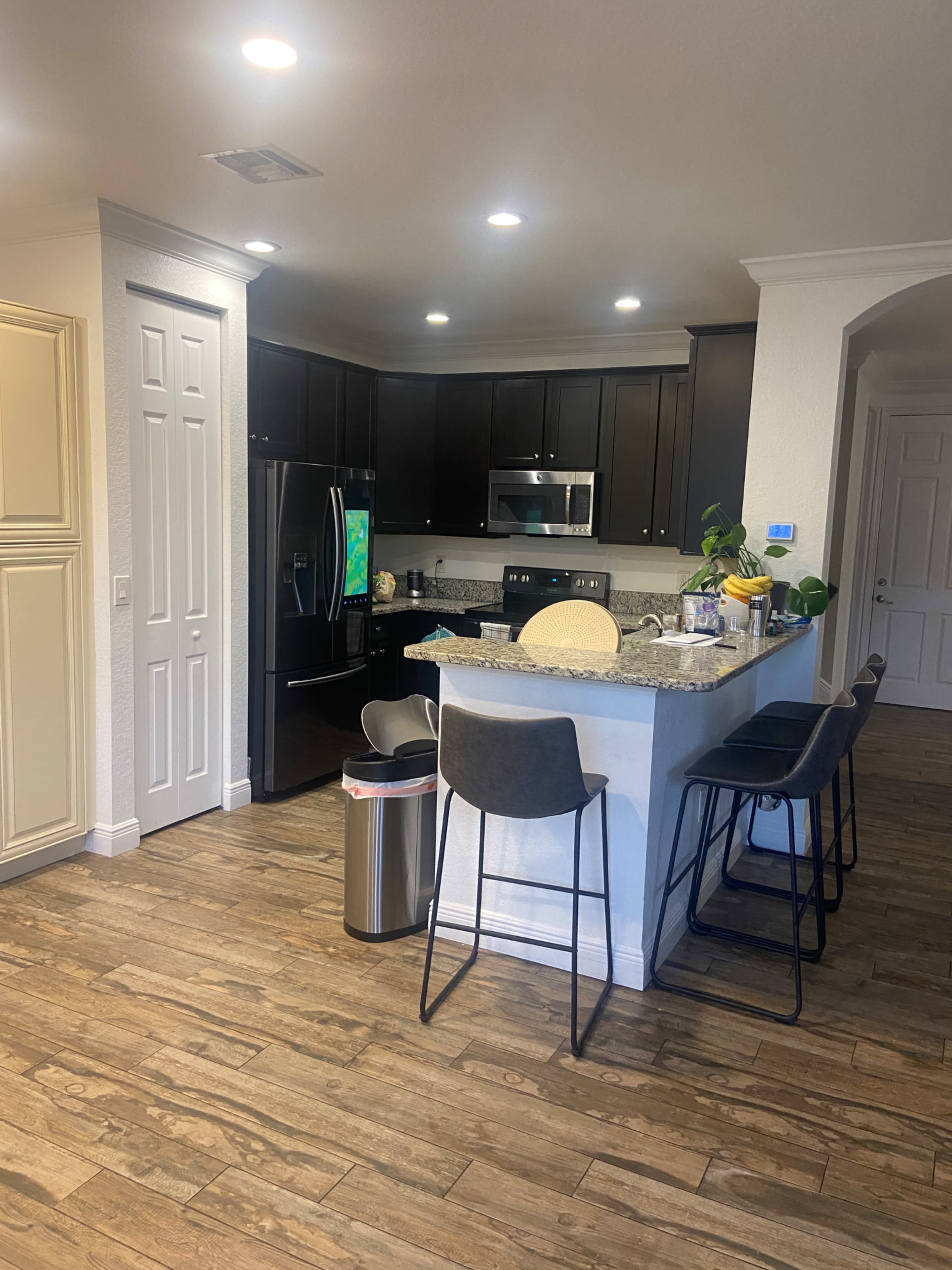 A modern kitchen with dark cabinetry, stainless steel appliances, a granite countertop, and bar stools along the island.