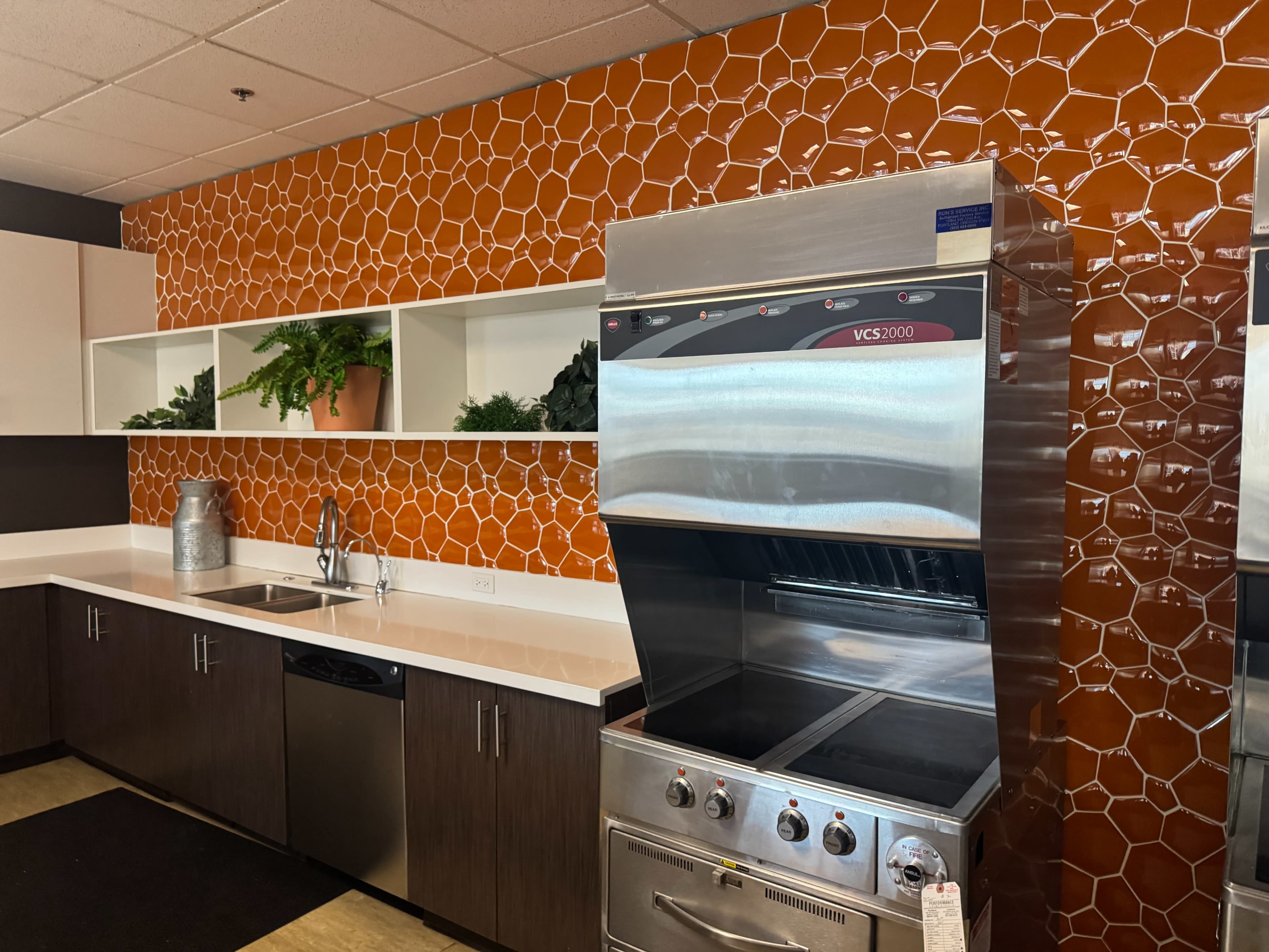 The image shows a modern kitchen with a stainless steel commercial stove, a sink, and an orange honeycomb tile backsplash.