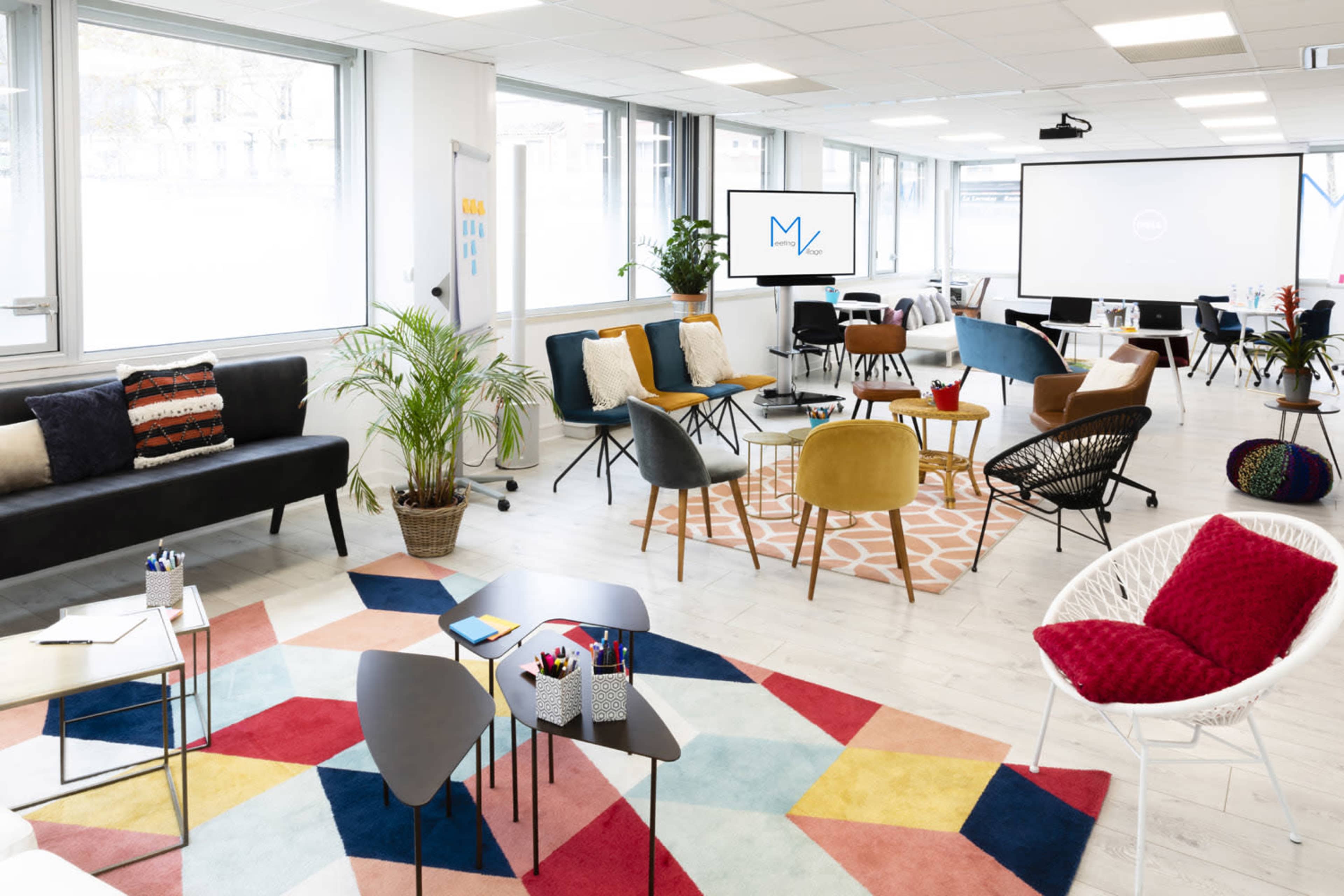 A modern office space with a variety of seating arrangements, colorful rugs, and presentation equipment.