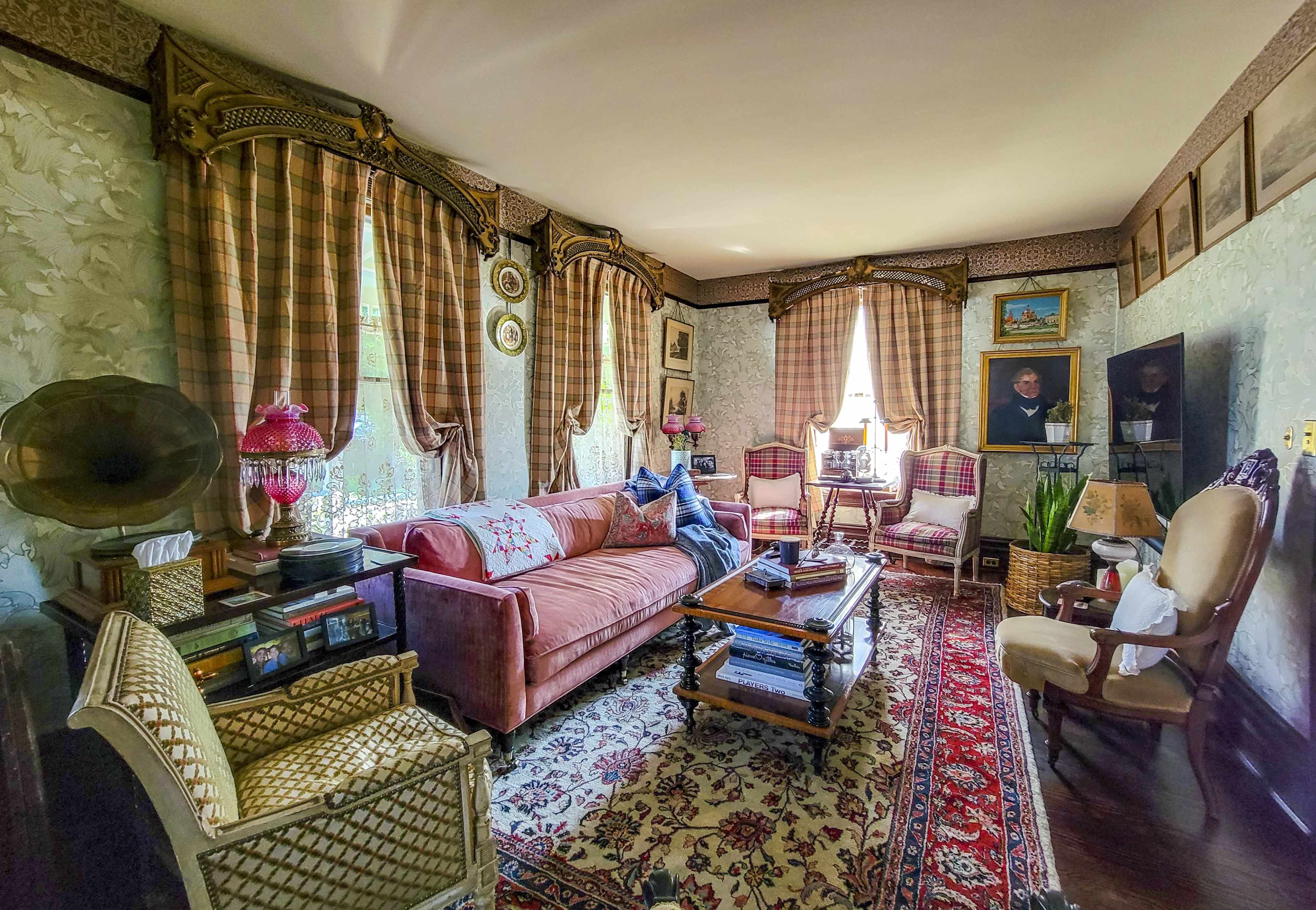 The image shows a vintage living room with a pink sofa, patterned curtains, and various decorative items, including a gramophone and framed artwork.