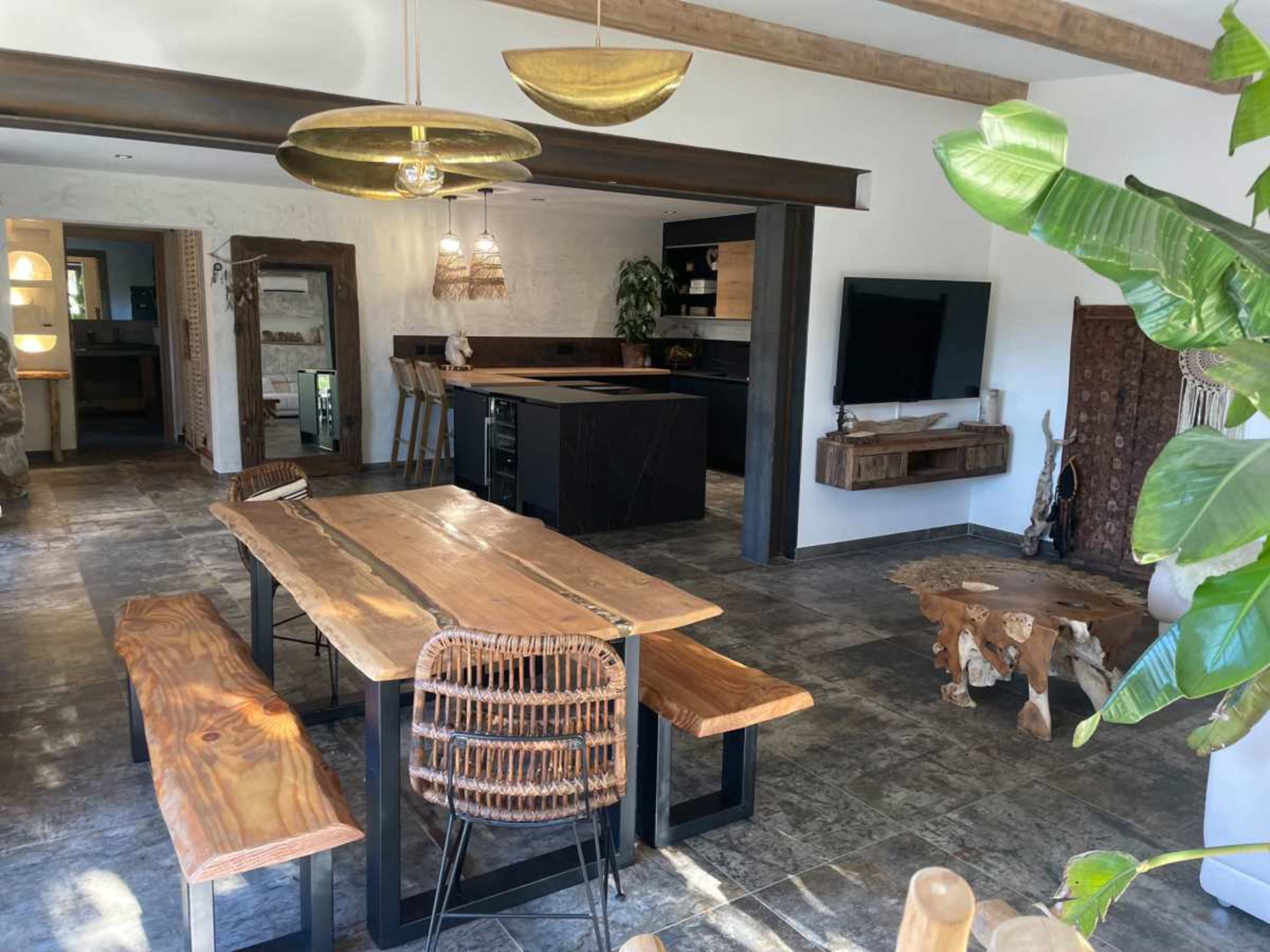 The image shows a modern open-concept living and dining area with a wooden table, comfortable seating, and a kitchen equipped with a large island.