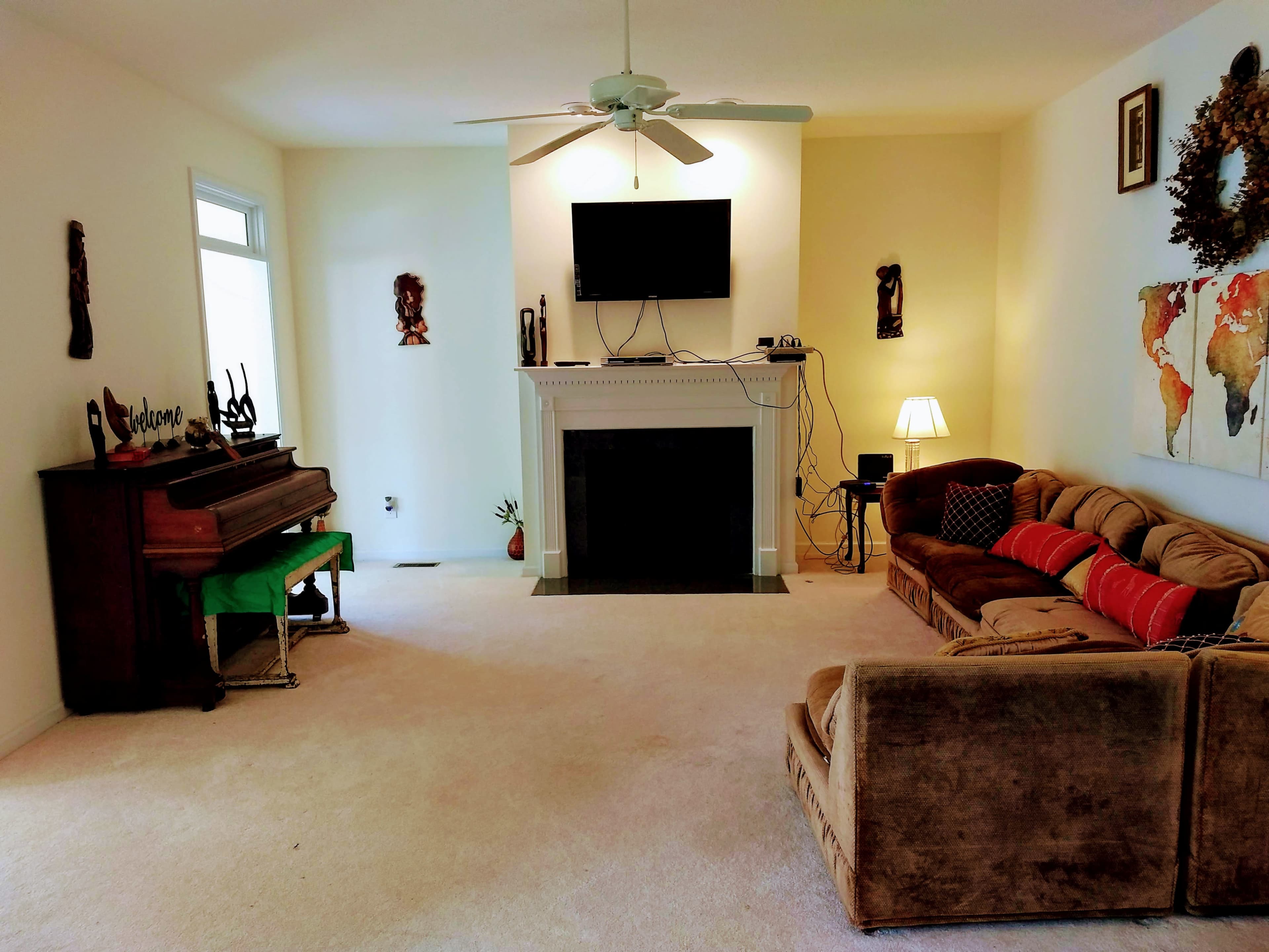 The room features a couch and a piano positioned near a fireplace, with a television mounted on the wall and a world map artwork.
