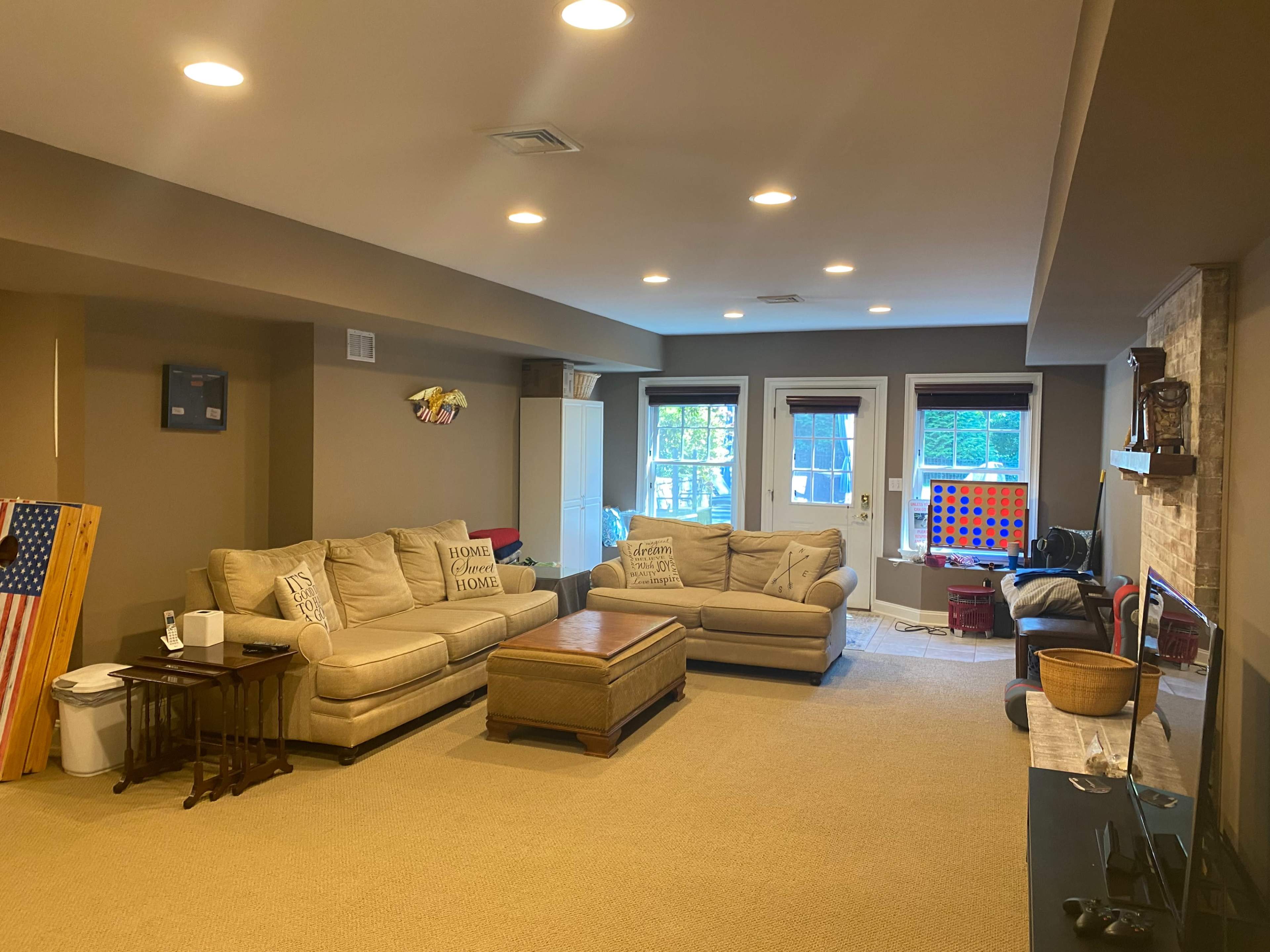 A spacious living room features a beige sofa set, a wooden coffee table, and multiple windows with natural light.