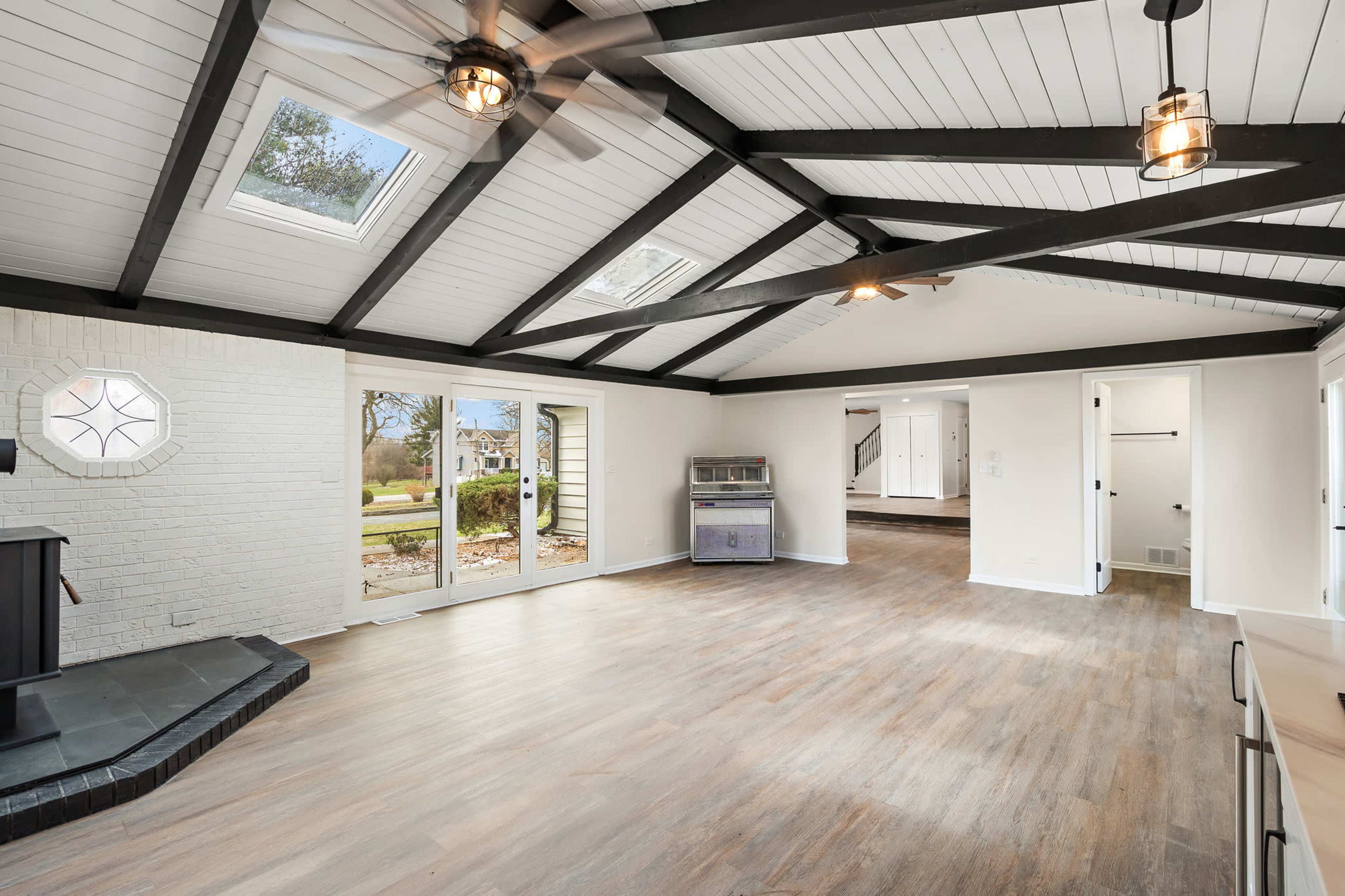 The image shows a spacious, open living area with a vaulted ceiling, large windows, and light-colored walls.