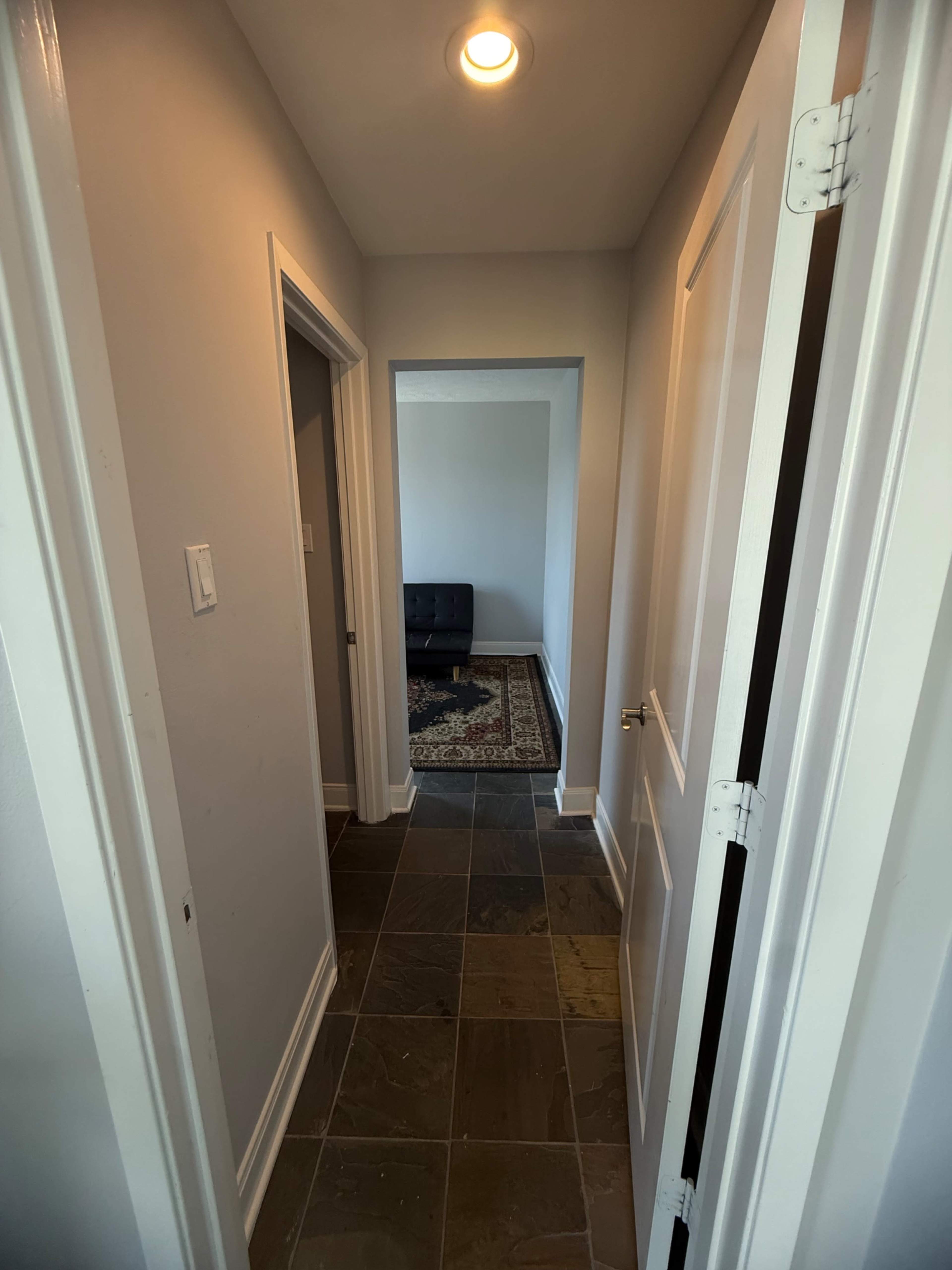 A well-lit hallway with tiled flooring leads to an open room at the end, flanked by two doors on either side.
