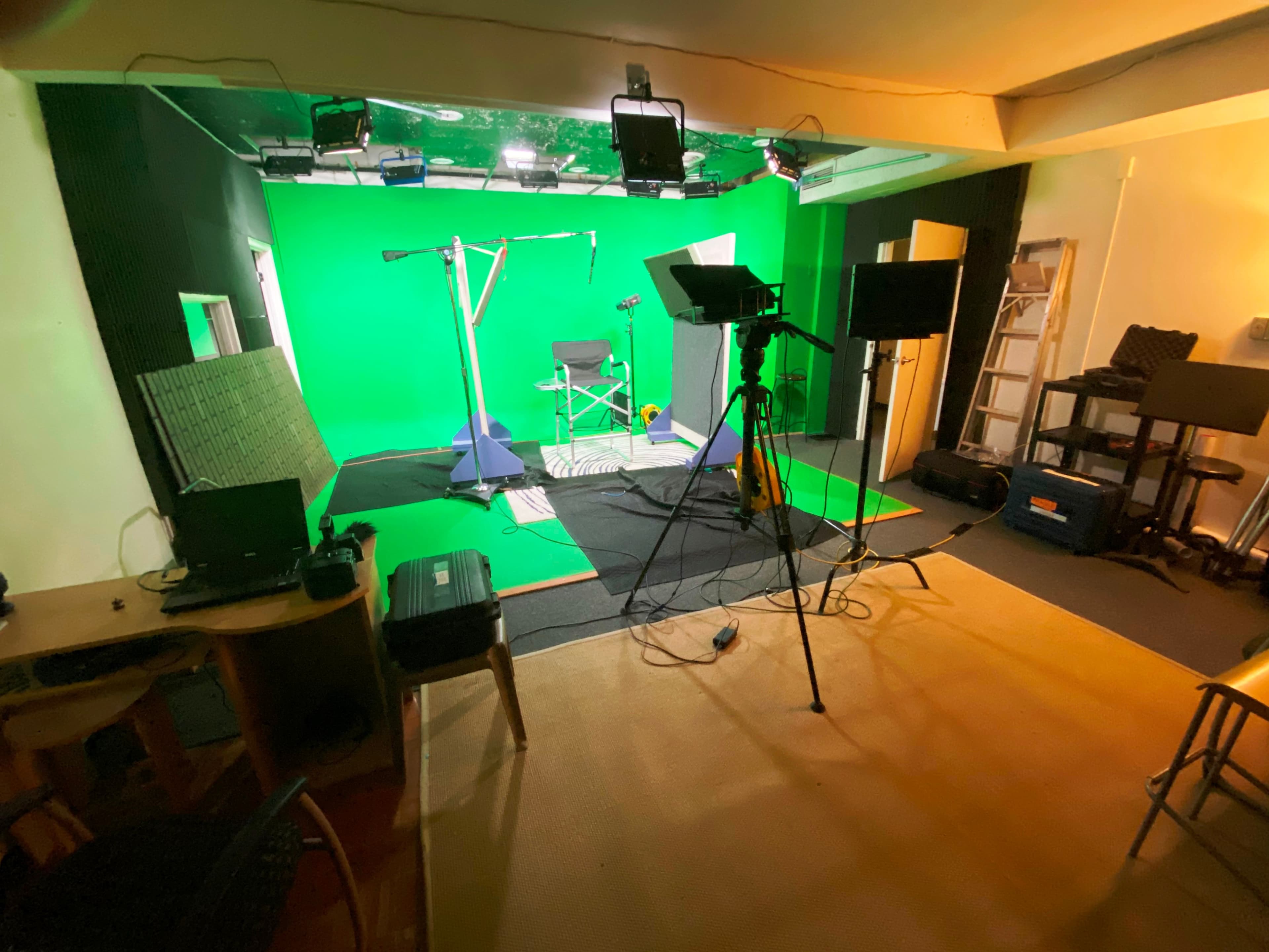 A recording studio with a green screen backdrop, lighting equipment, and various electrical cables arranged on the floor.