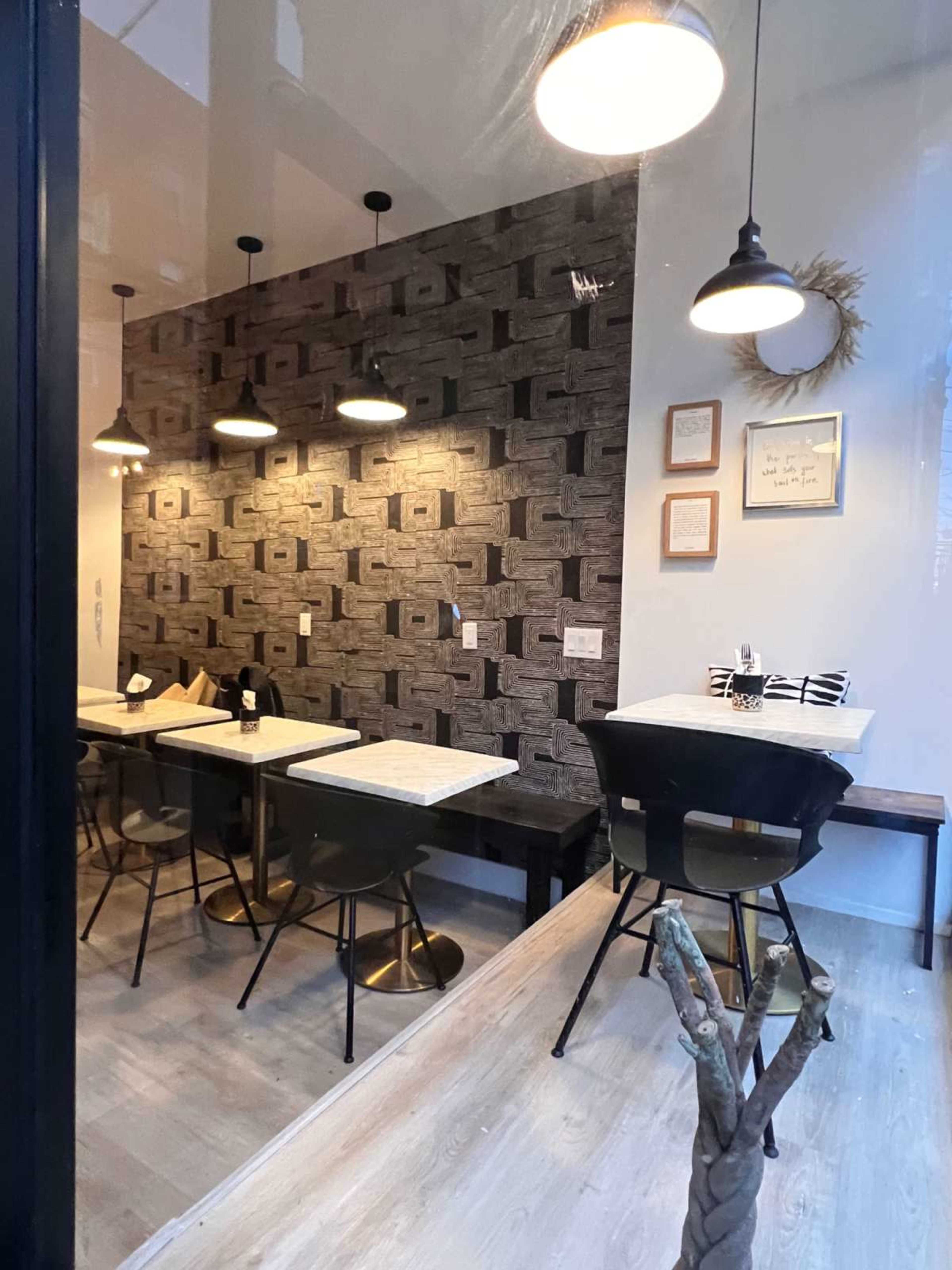 The image shows a modern café interior with patterned wallpaper, wooden tables, and black chairs, illuminated by hanging pendant lights.