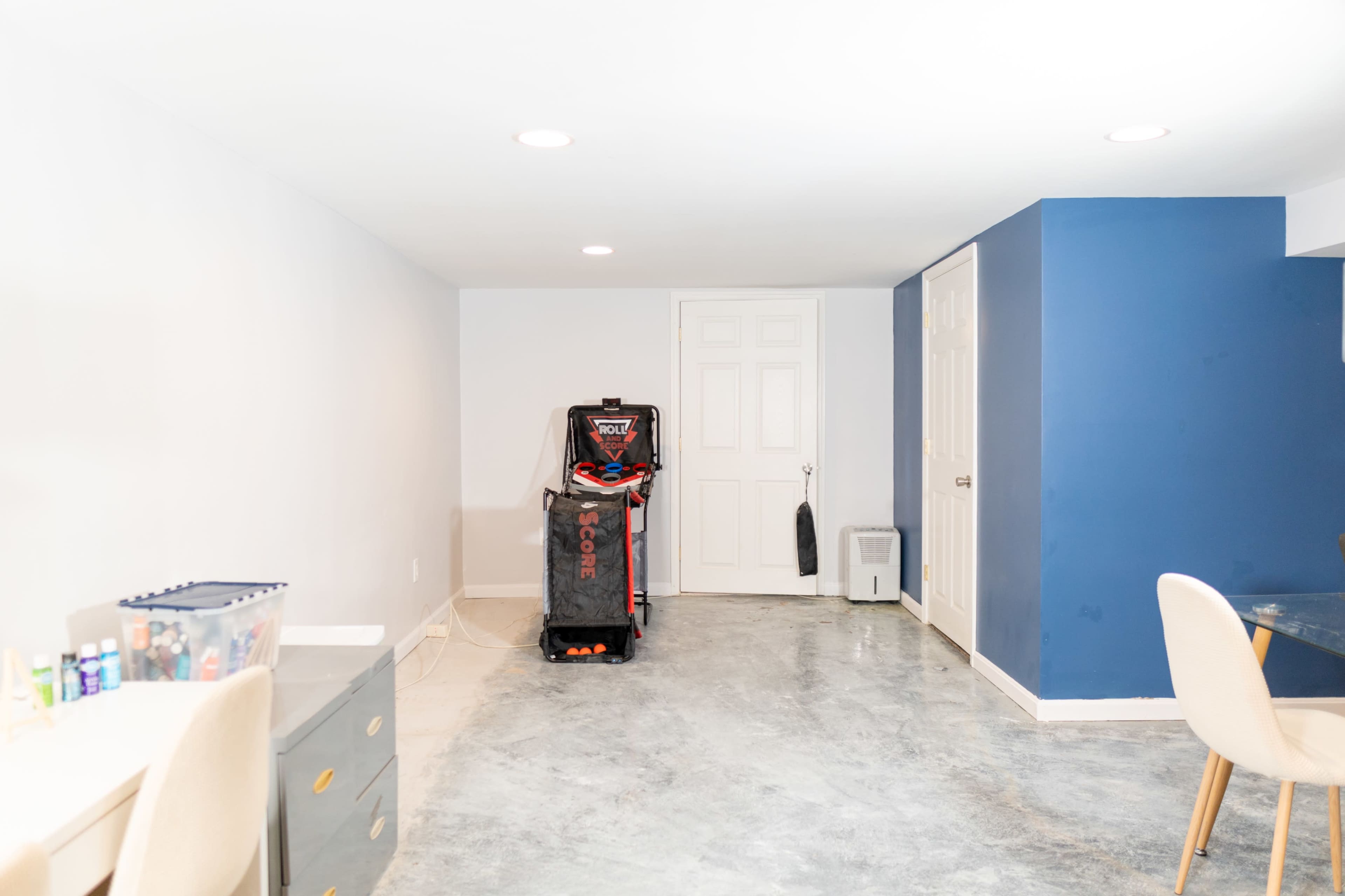 The image shows a spacious basement room with a gray concrete floor, a blue accent wall, and a storage unit in the corner.