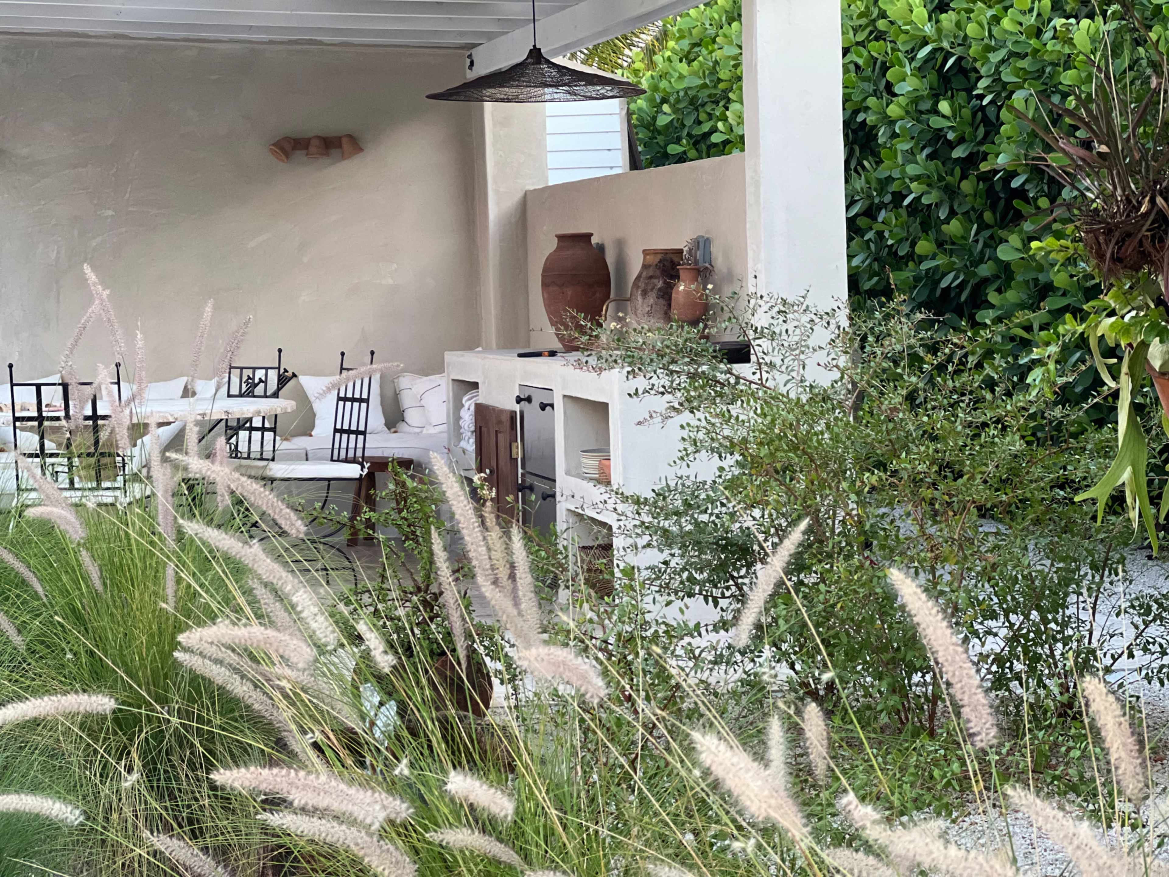 A cozy outdoor kitchen area is framed by lush greenery and features rustic decor, including pottery and seating.
