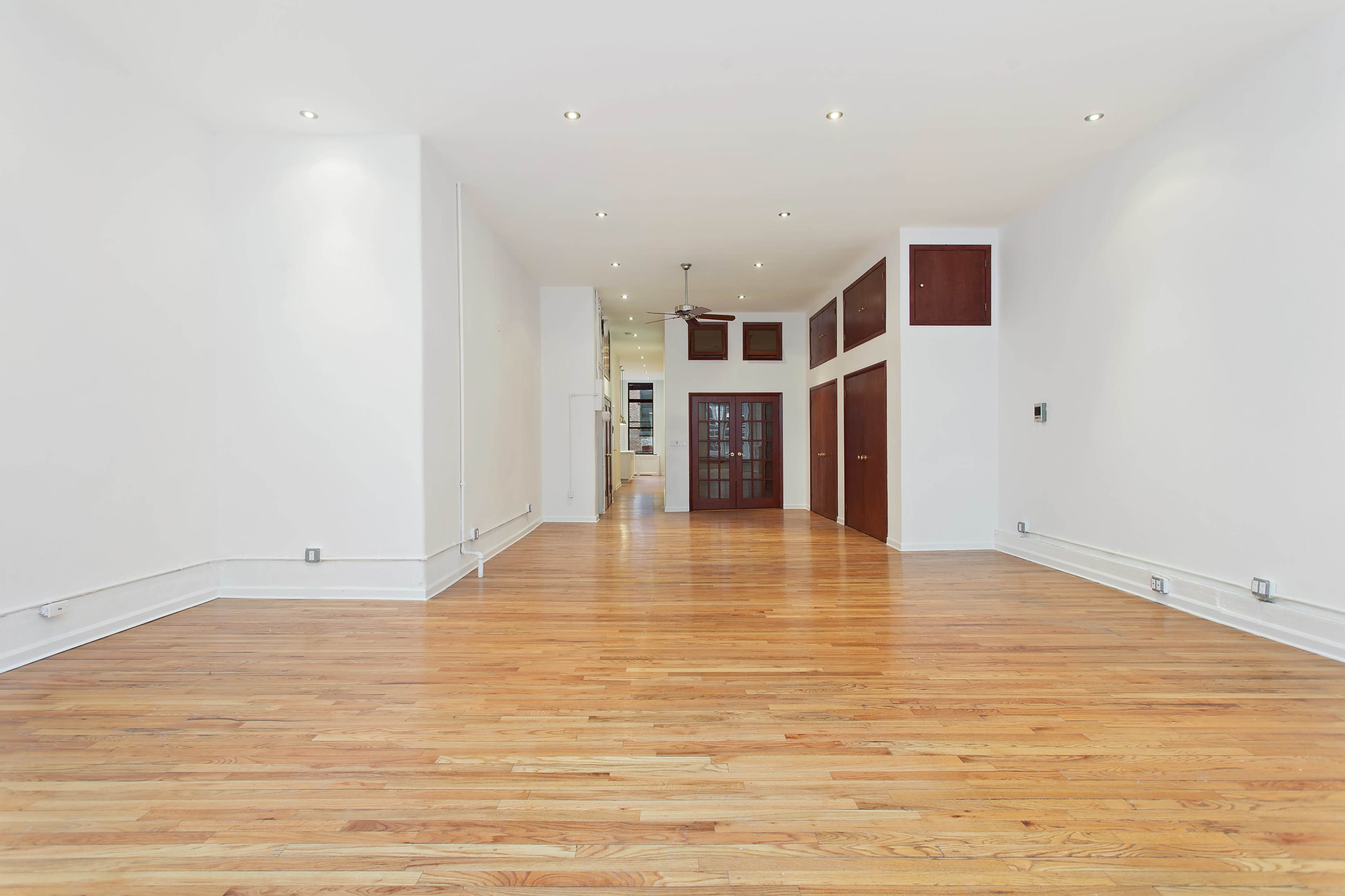 A spacious, empty room with wooden flooring and white walls, featuring recessed lighting and a ceiling fan.