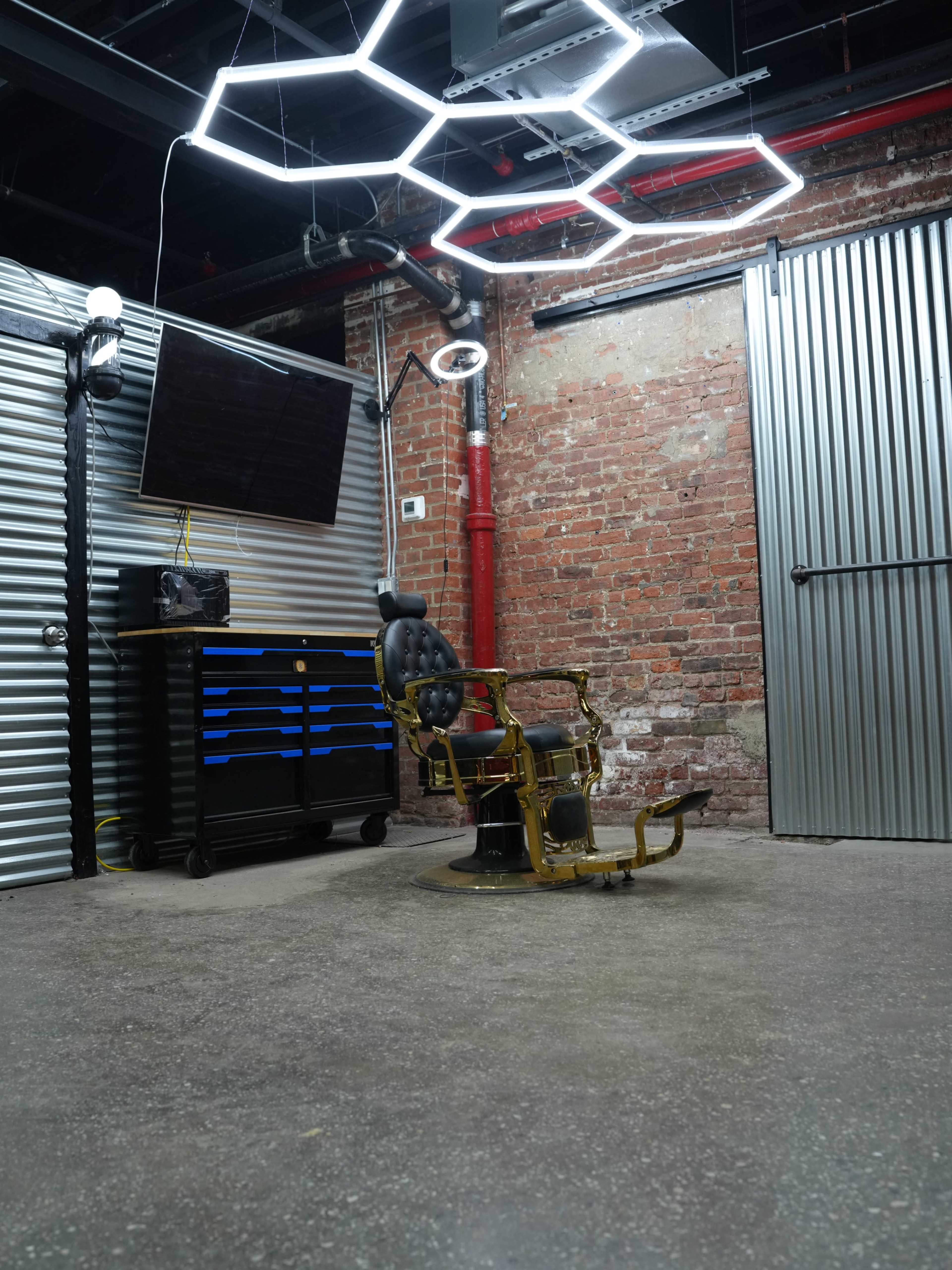 The image shows a vintage barber chair positioned in an industrial-style room with exposed brick walls and metal paneling.