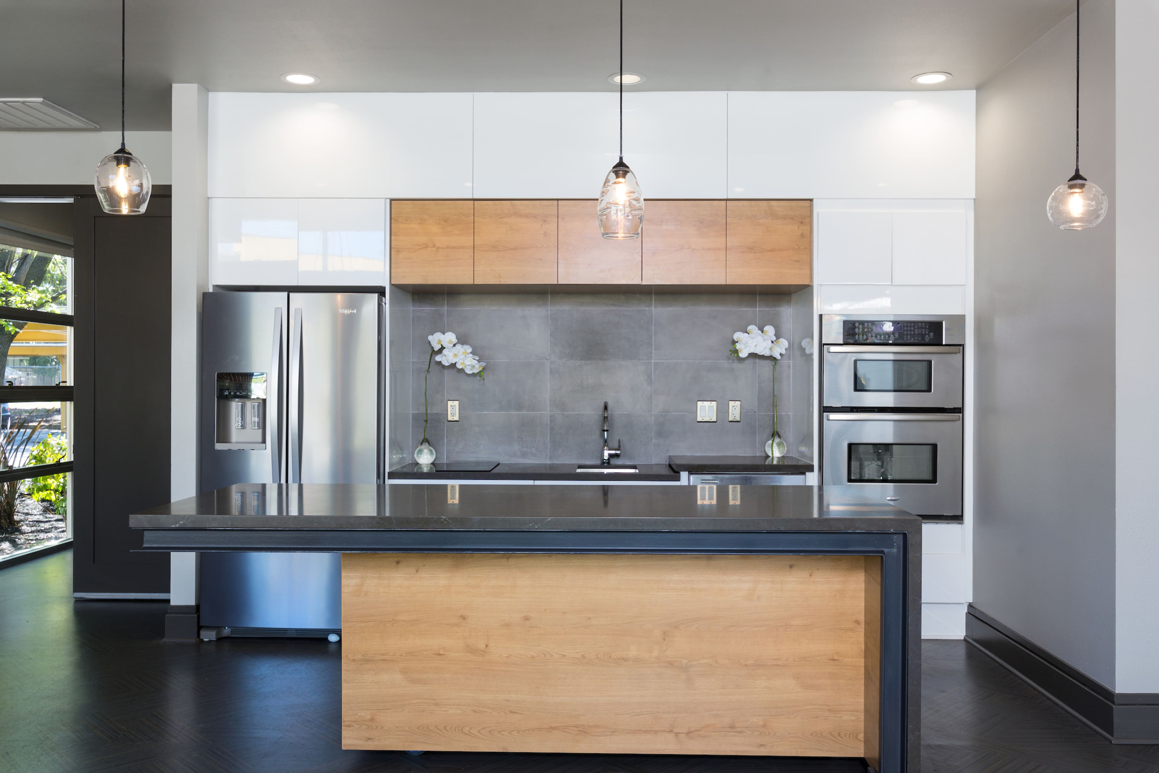 A modern kitchen features a central island with a wooden base, sleek countertops, stainless steel appliances, and a minimalist cabinetry design.