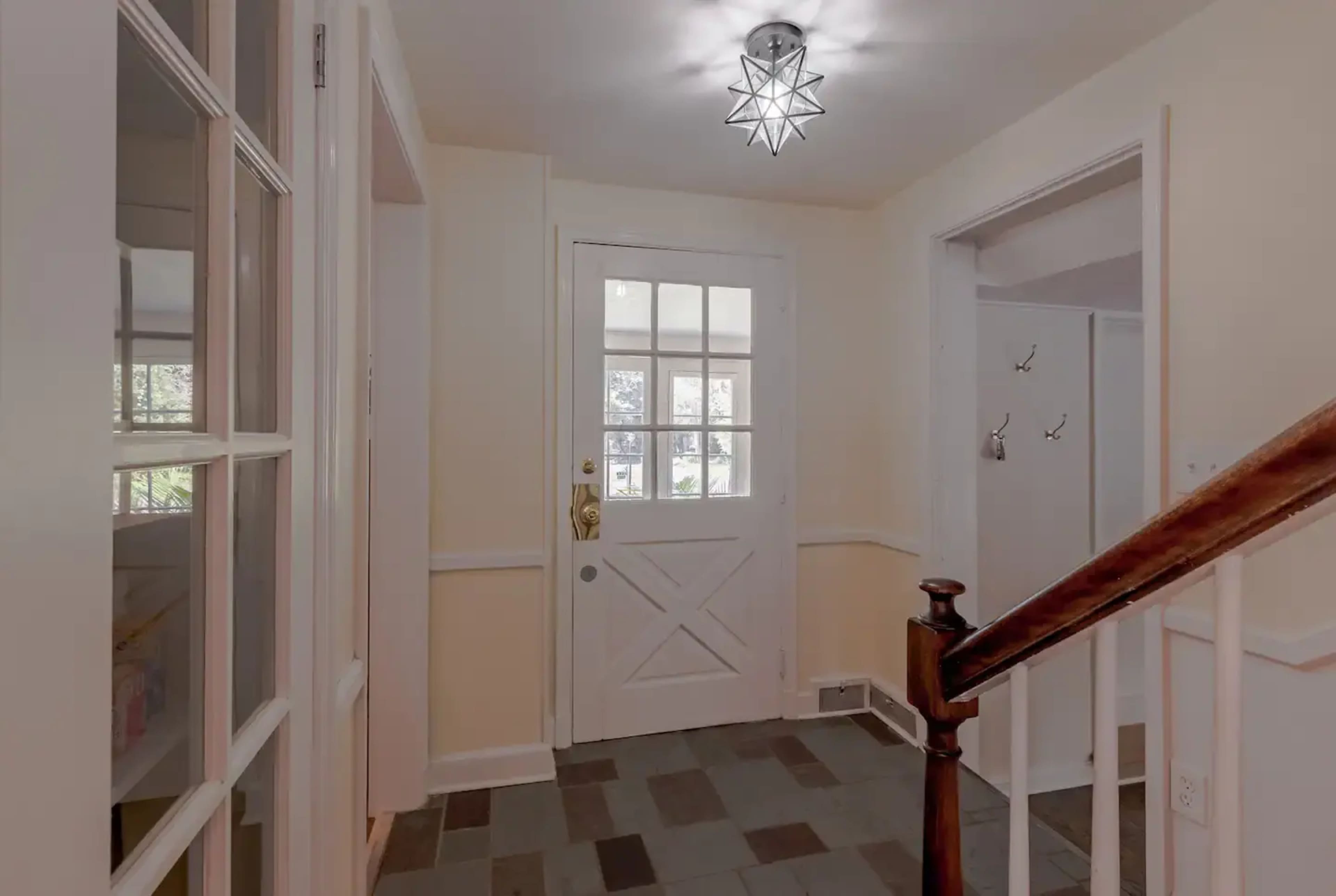 A bright entryway with a front door featuring multiple panes of glass, alongside a staircase and a coat rack.