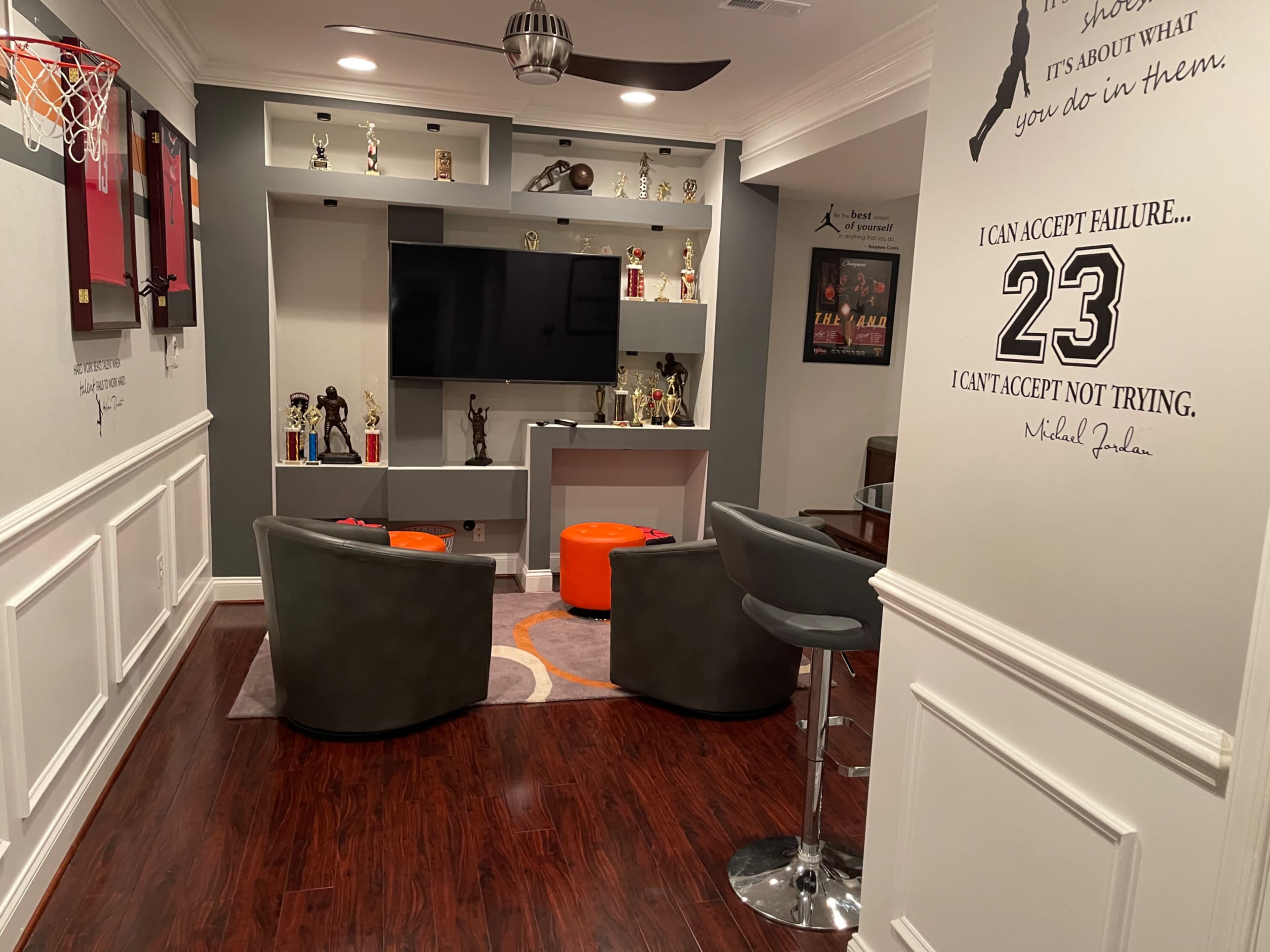 A well-decorated recreational room featuring a television, trophies, a small basketball hoop, and seating arranged around an orange and gray carpet.