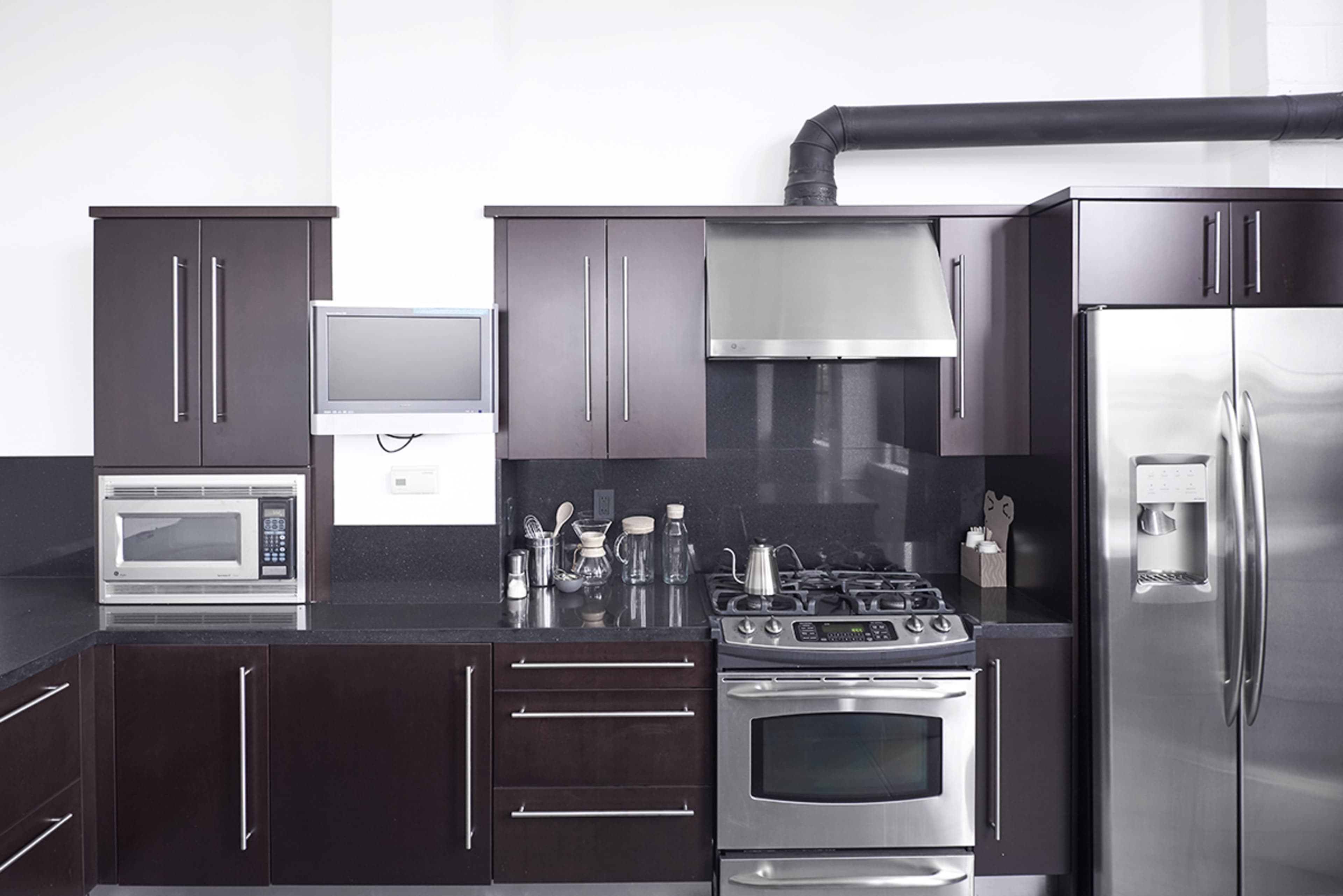 The kitchen features dark wooden cabinets, stainless steel appliances, a gas stove, and a countertop with a microwave and various glass containers.