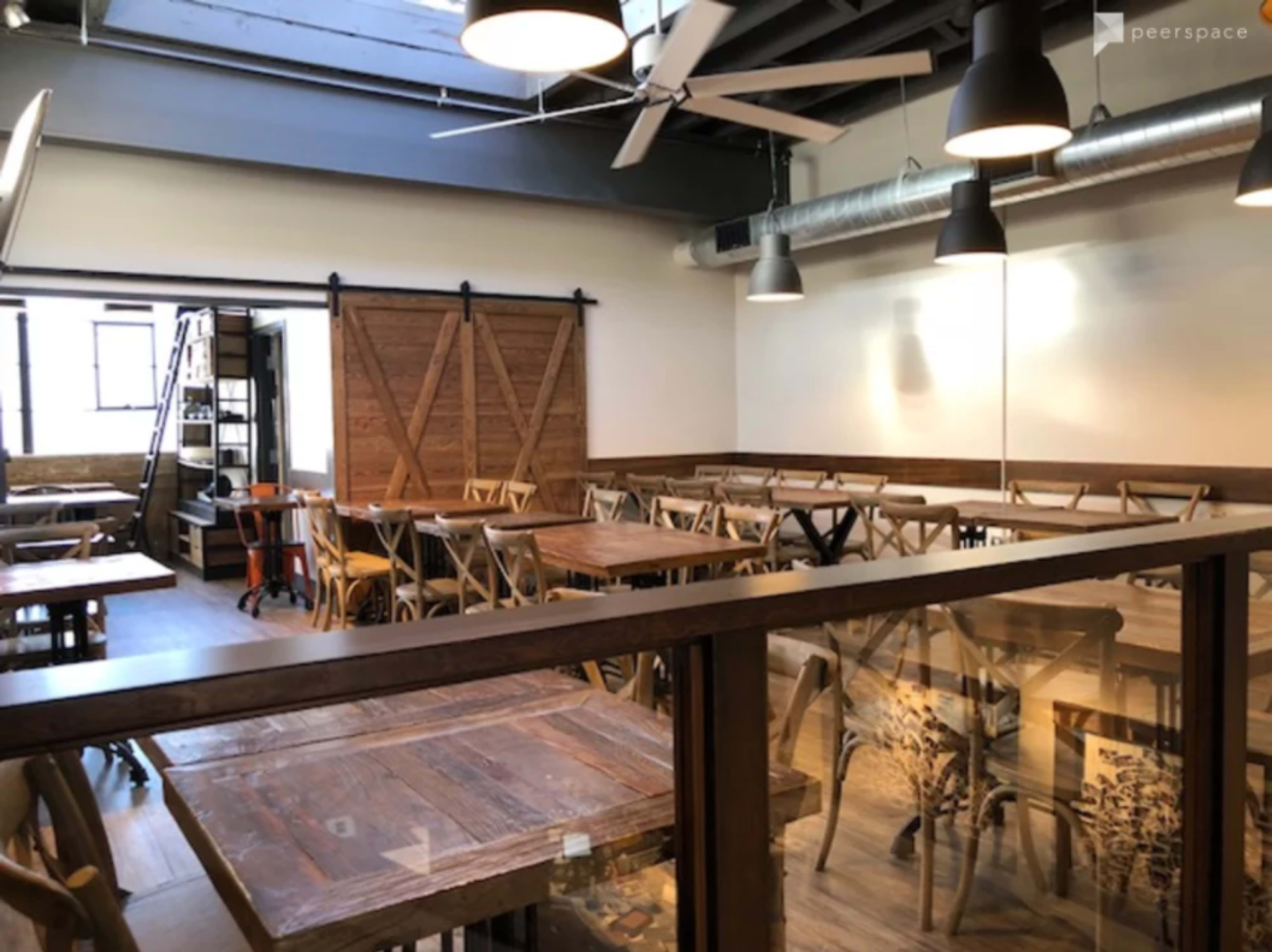 An empty restaurant interior with wooden tables and chairs, a sliding barn door, and industrial-style lighting.
