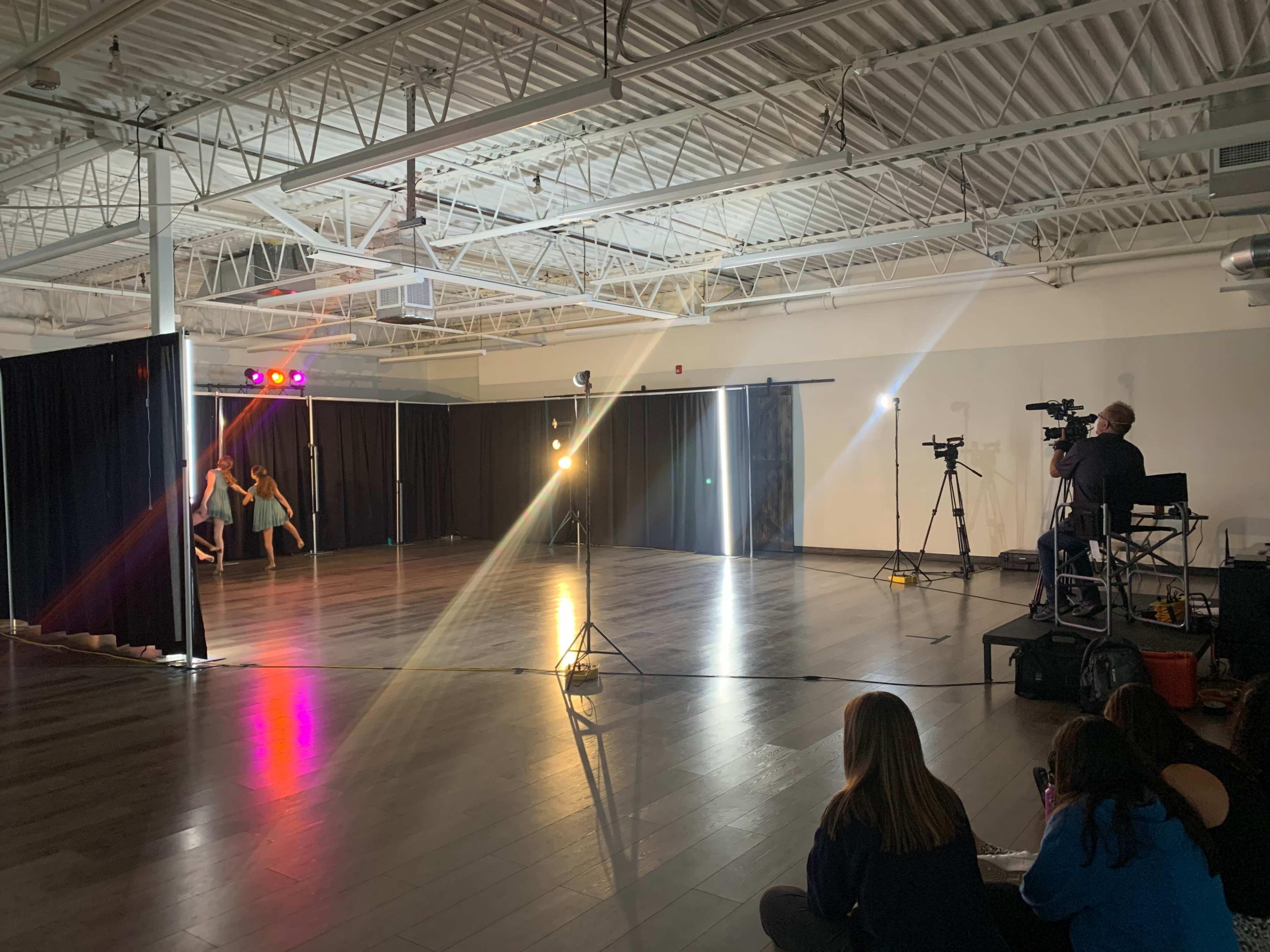 A dance rehearsal takes place in a spacious studio with cameras set up to capture the performance.