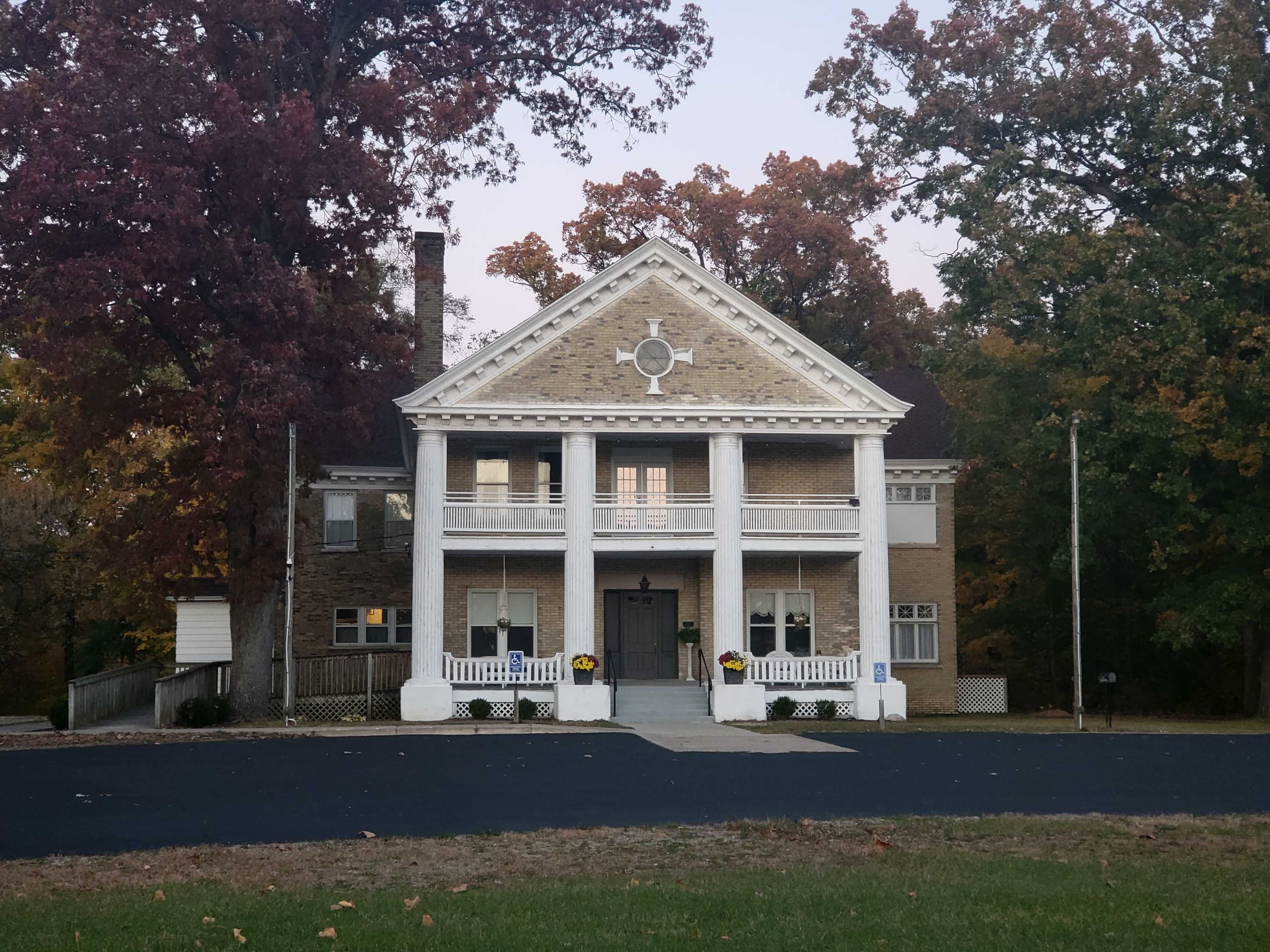 A large, two-story brick house with white columns and a porch, surrounded by autumn foliage.