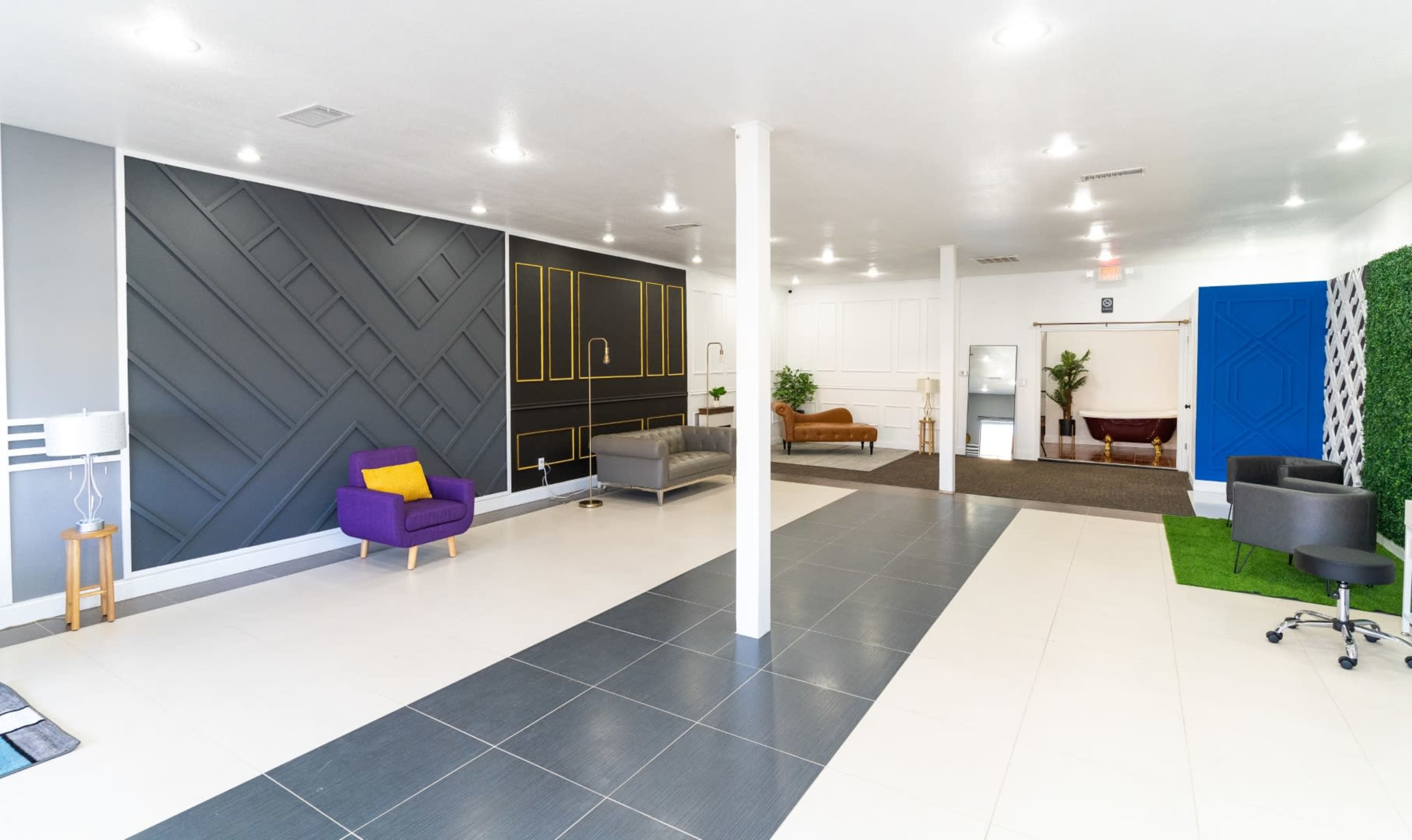 The image shows a spacious, modern interior featuring a mix of dark and light wall designs, stylish seating areas, and green accents.