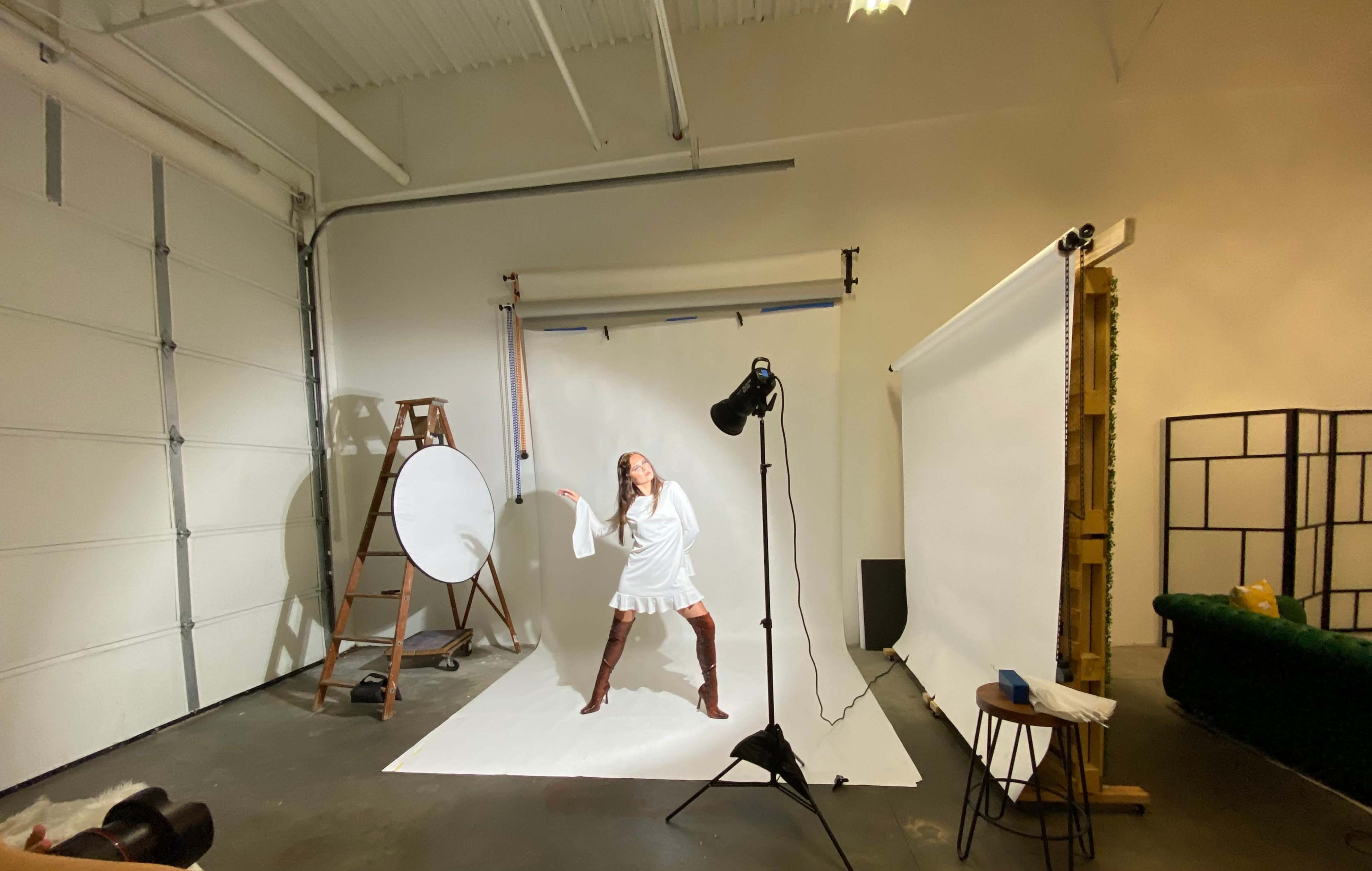 A model poses on a white backdrop in a photography studio equipped with various lighting and props.