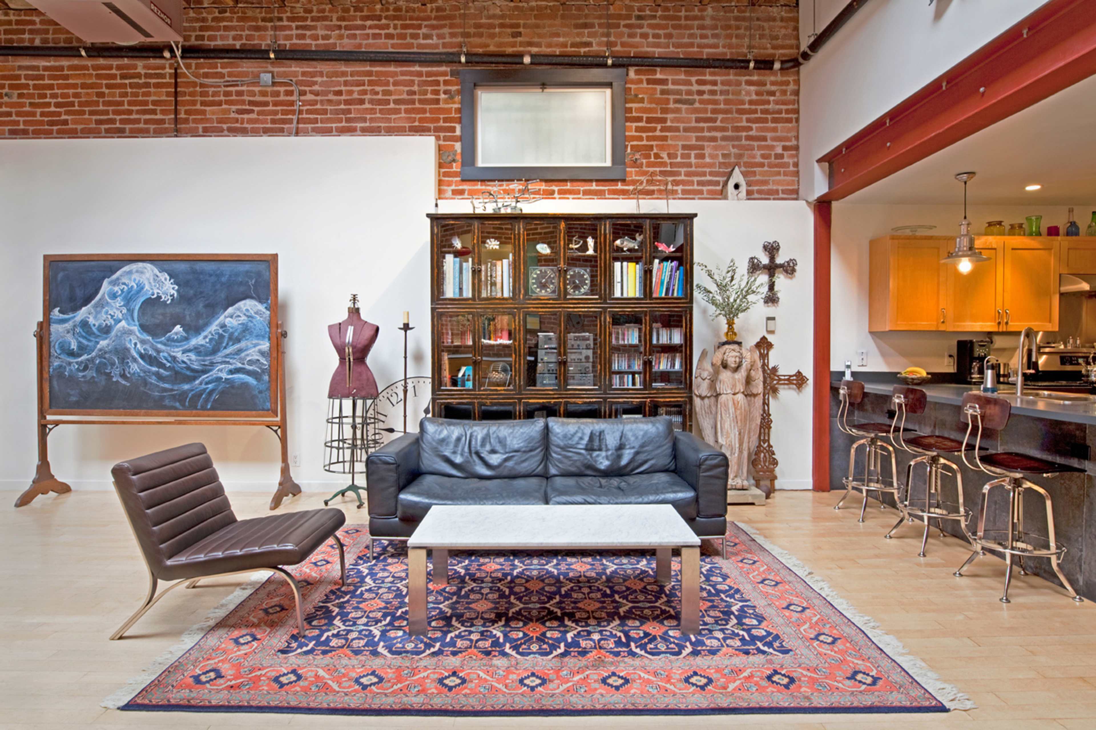 A modern living area features a black leather sofa, a marble coffee table, a large blue wave painting, and a combination of wooden and metal furnishings.