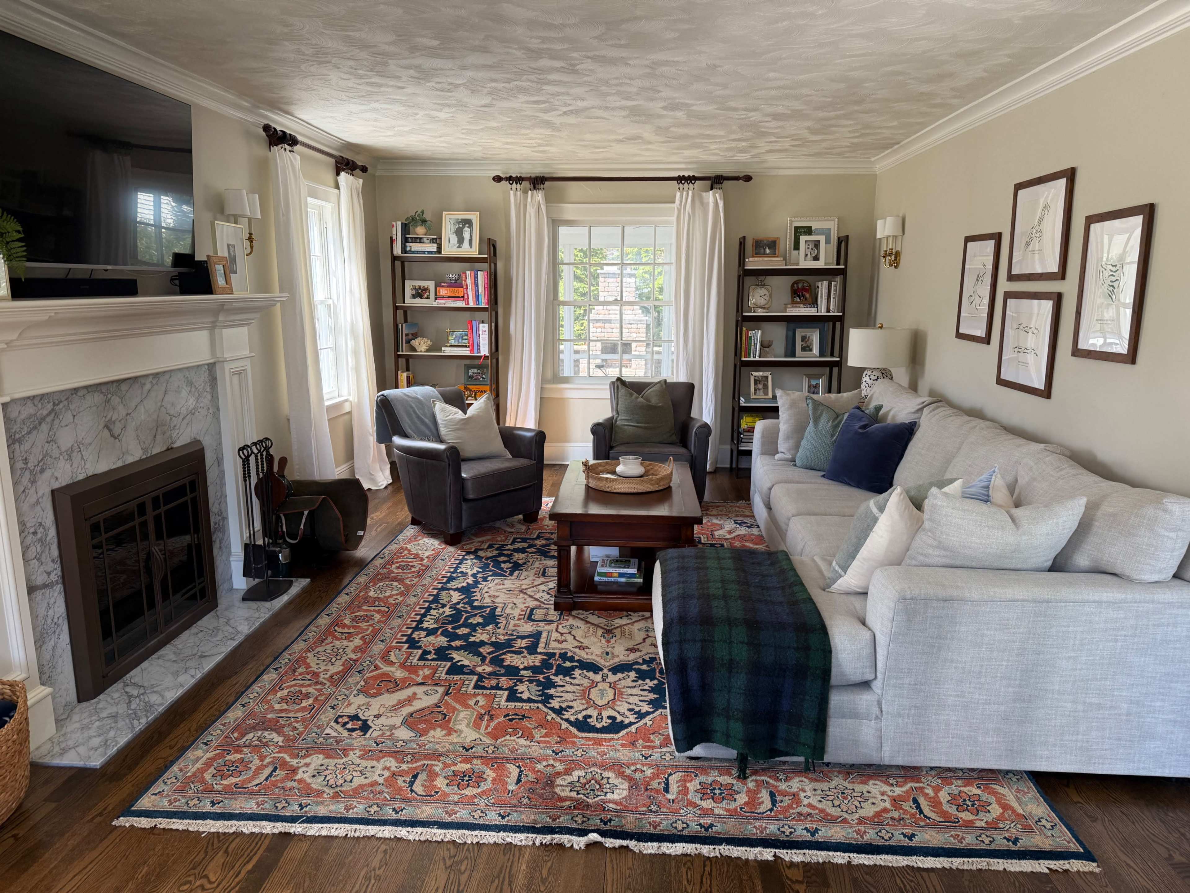 The living room features a gray sofa and armchairs arranged around a wooden coffee table, with a decorative rug and a fireplace on one wall.