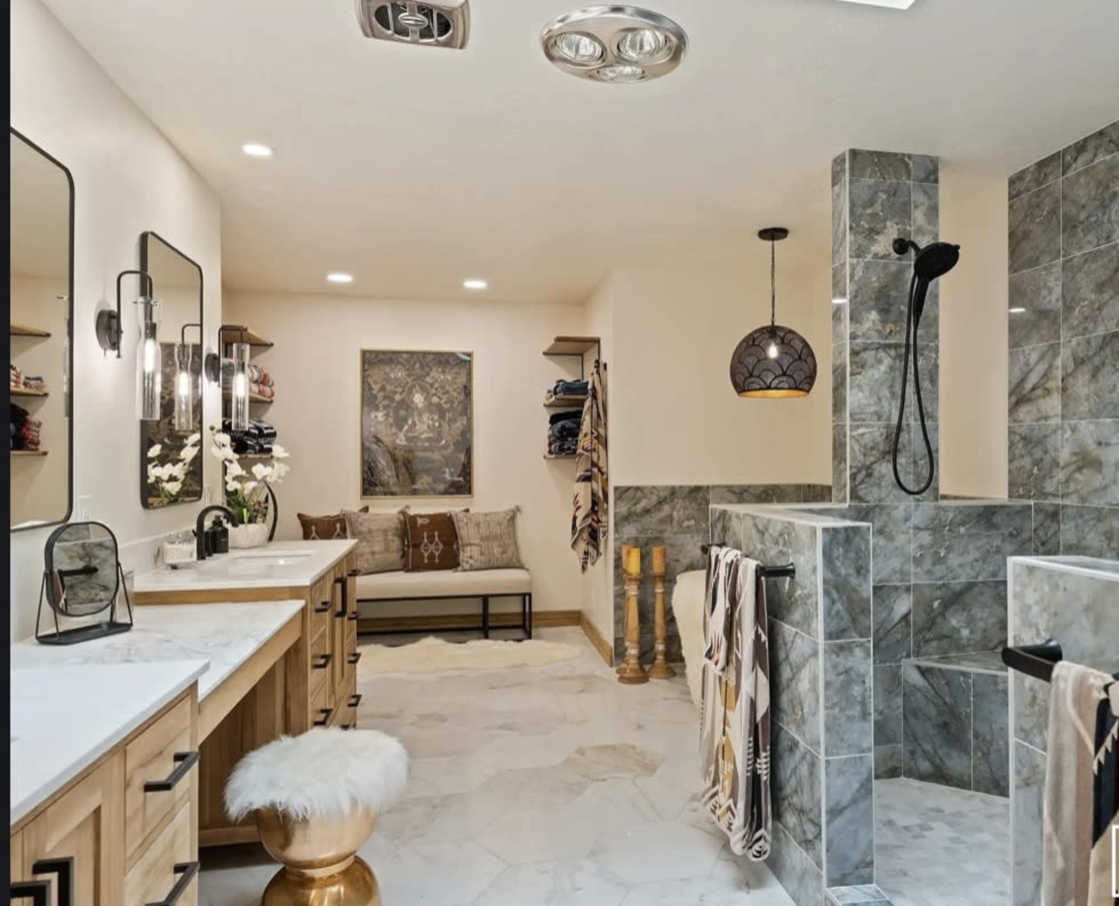 The image shows a modern bathroom featuring dual vanities, a shower area, and a sitting space with decorative towels.