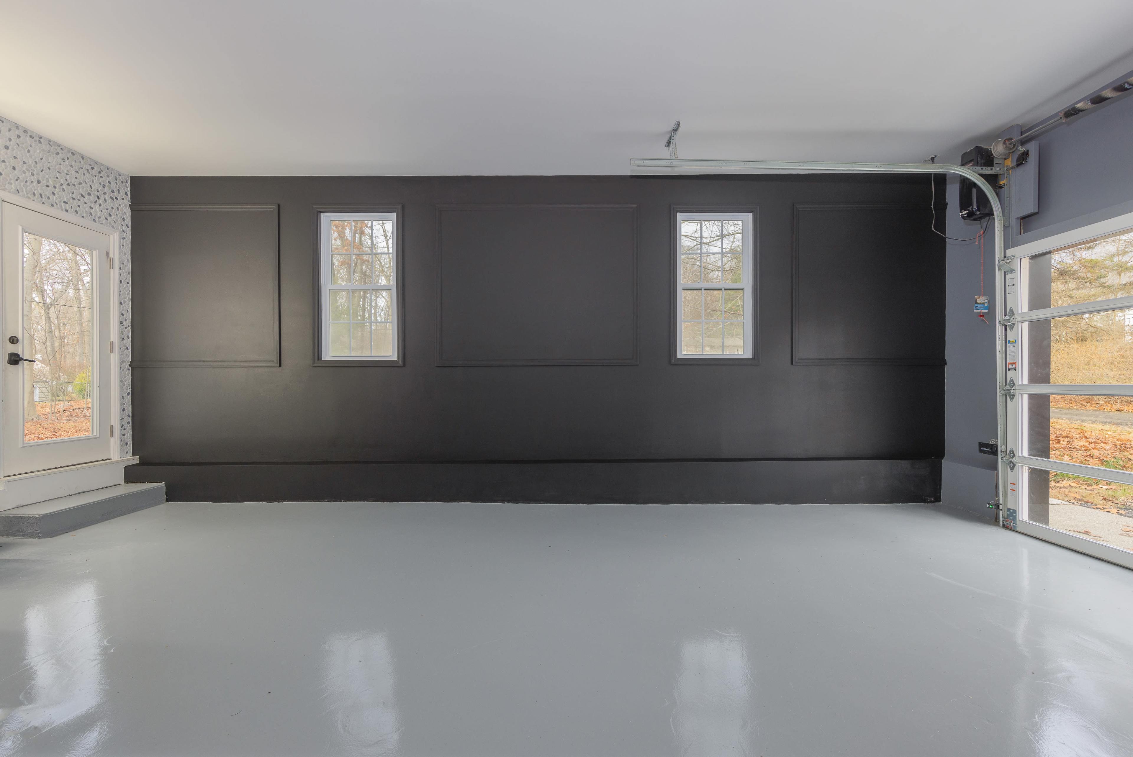A spacious garage with a polished floor, black accent wall, two windows, and a roll-up garage door.