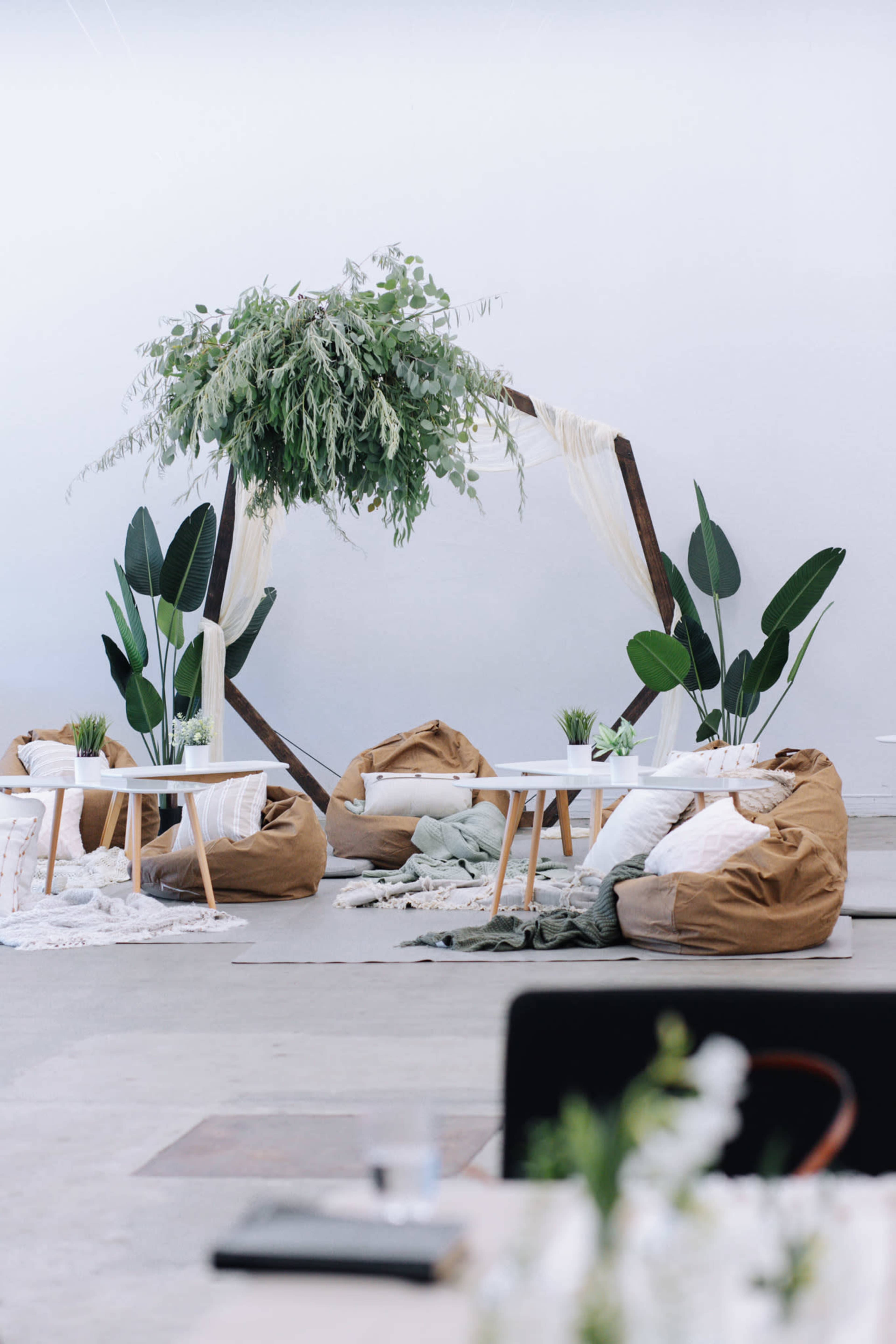 A modern event space featuring bean bag seating, small tables, and a decorative arch adorned with greenery.