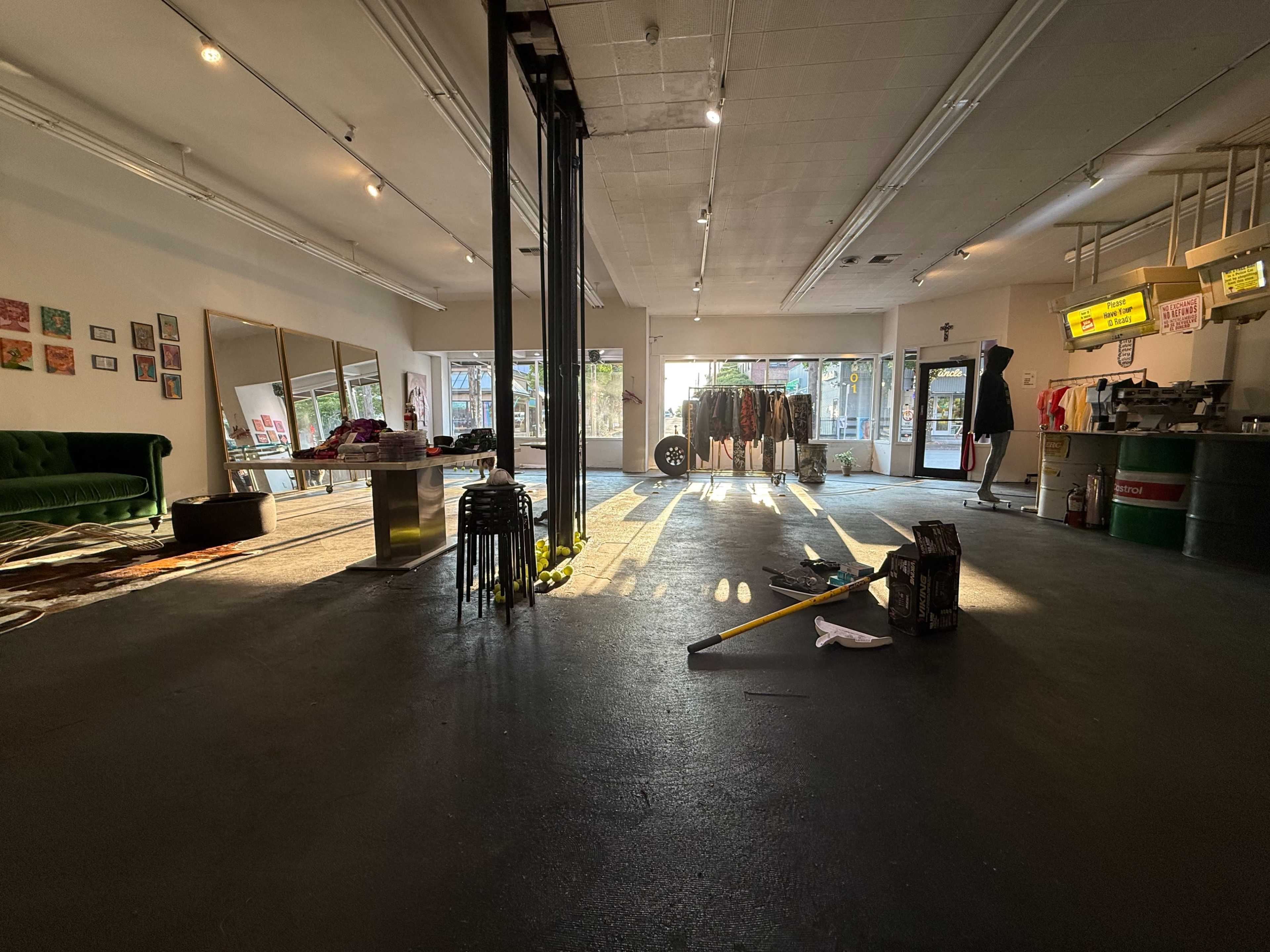 The image shows a spacious retail store with a green couch, a large mirror, clothing racks, and scattered items on the floor.