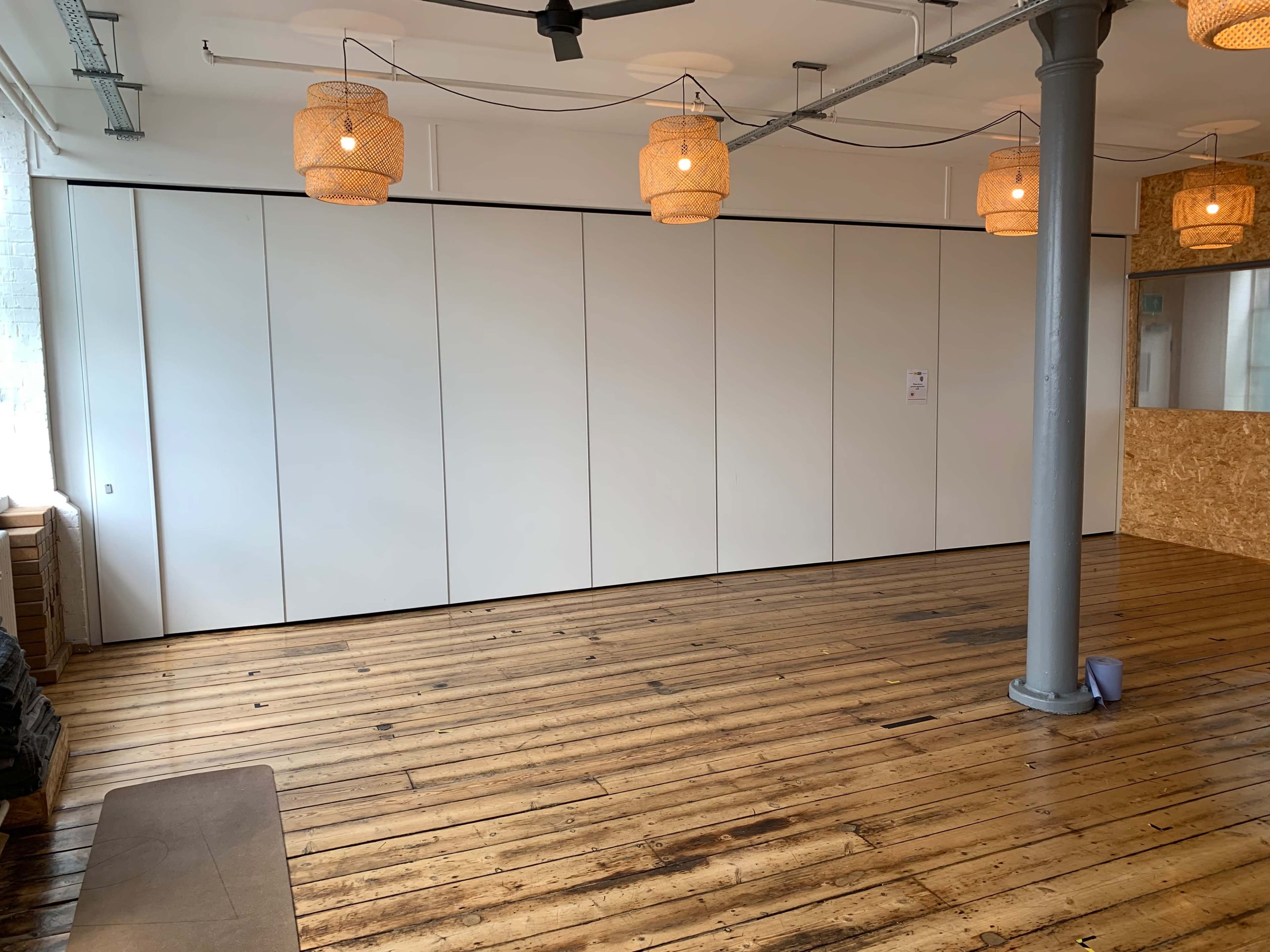 A spacious room with wooden floors, white paneling on one wall, and several pendant lights hanging from the ceiling.
