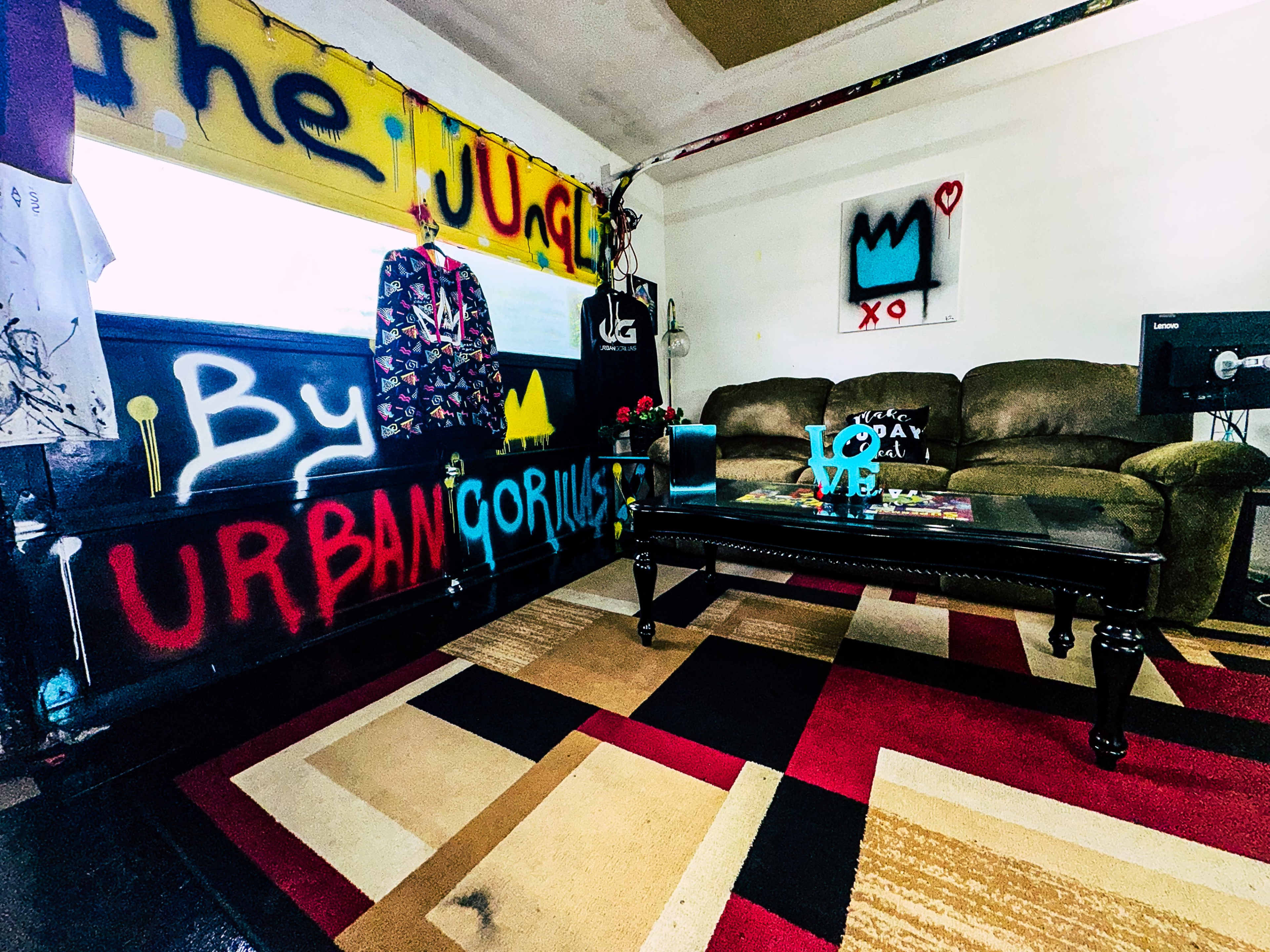 A creatively decorated room featuring graffiti on the walls, a brown sofa, and a coffee table on a multicolored rug.
