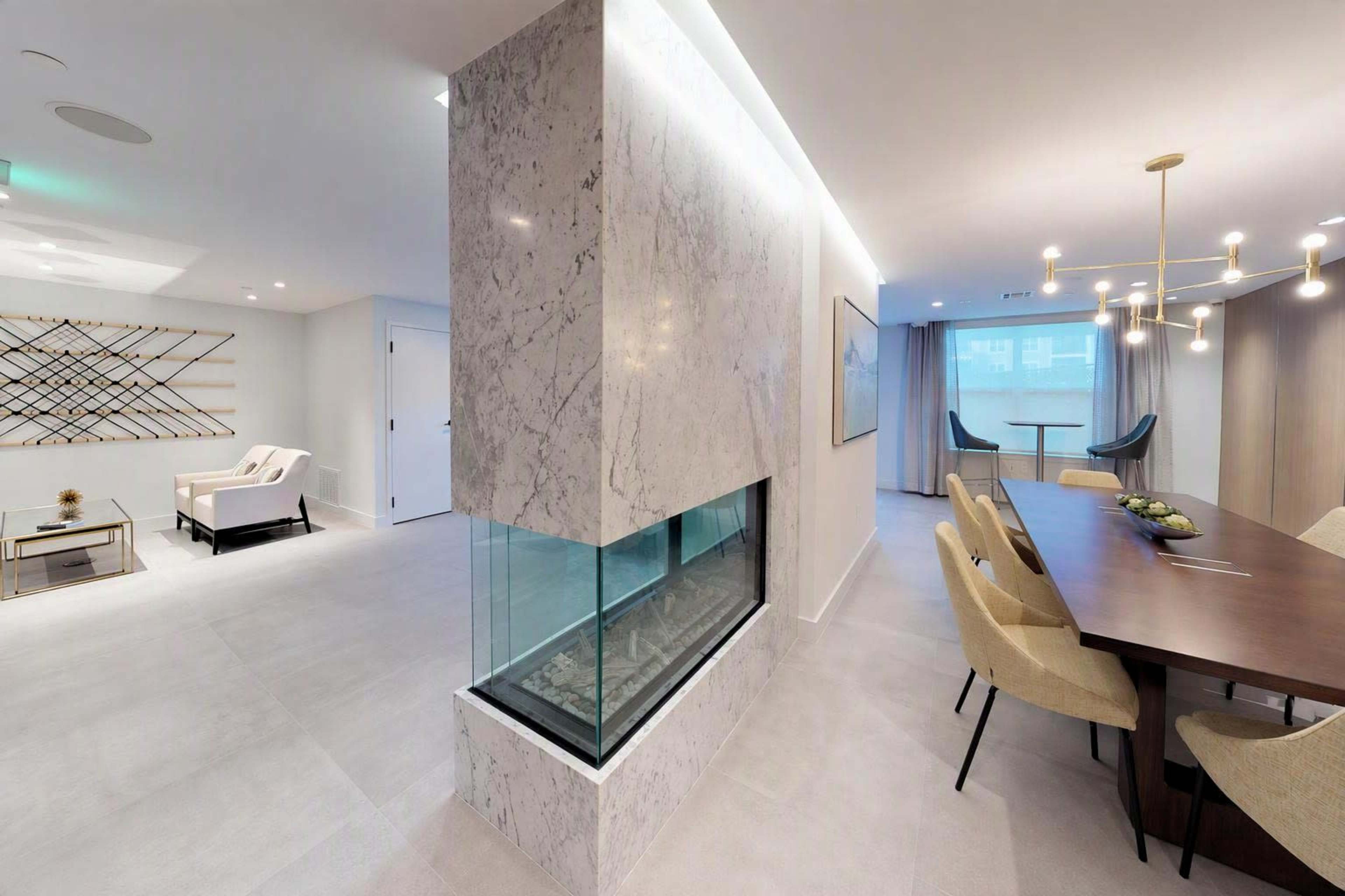 The image shows a modern interior featuring a sleek marble partition with a built-in fireplace, connecting a dining area to a living space.
