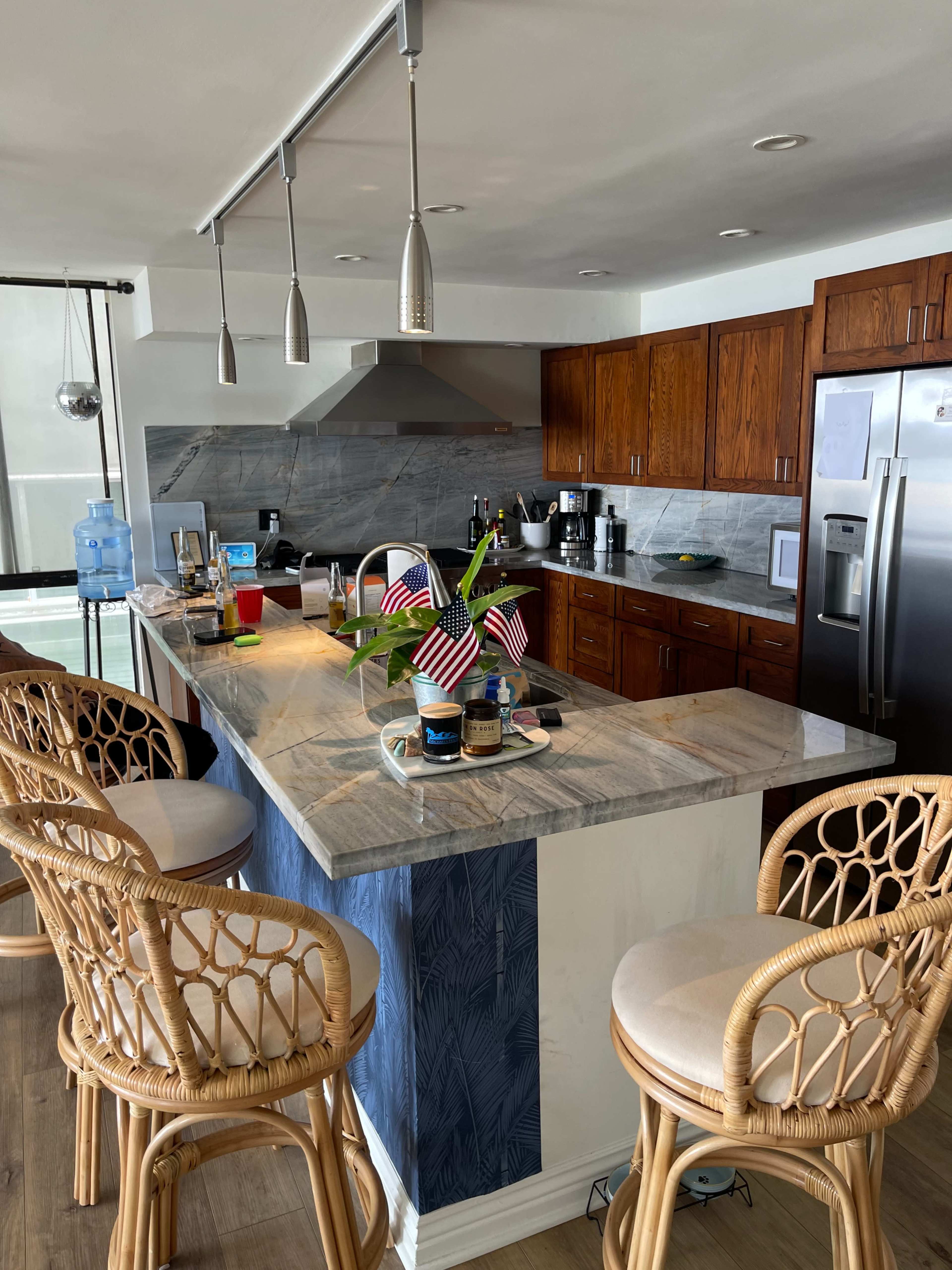 A modern kitchen with a marble island, wooden cabinets, and bar stools, featuring decorations and various kitchen items on the counter.