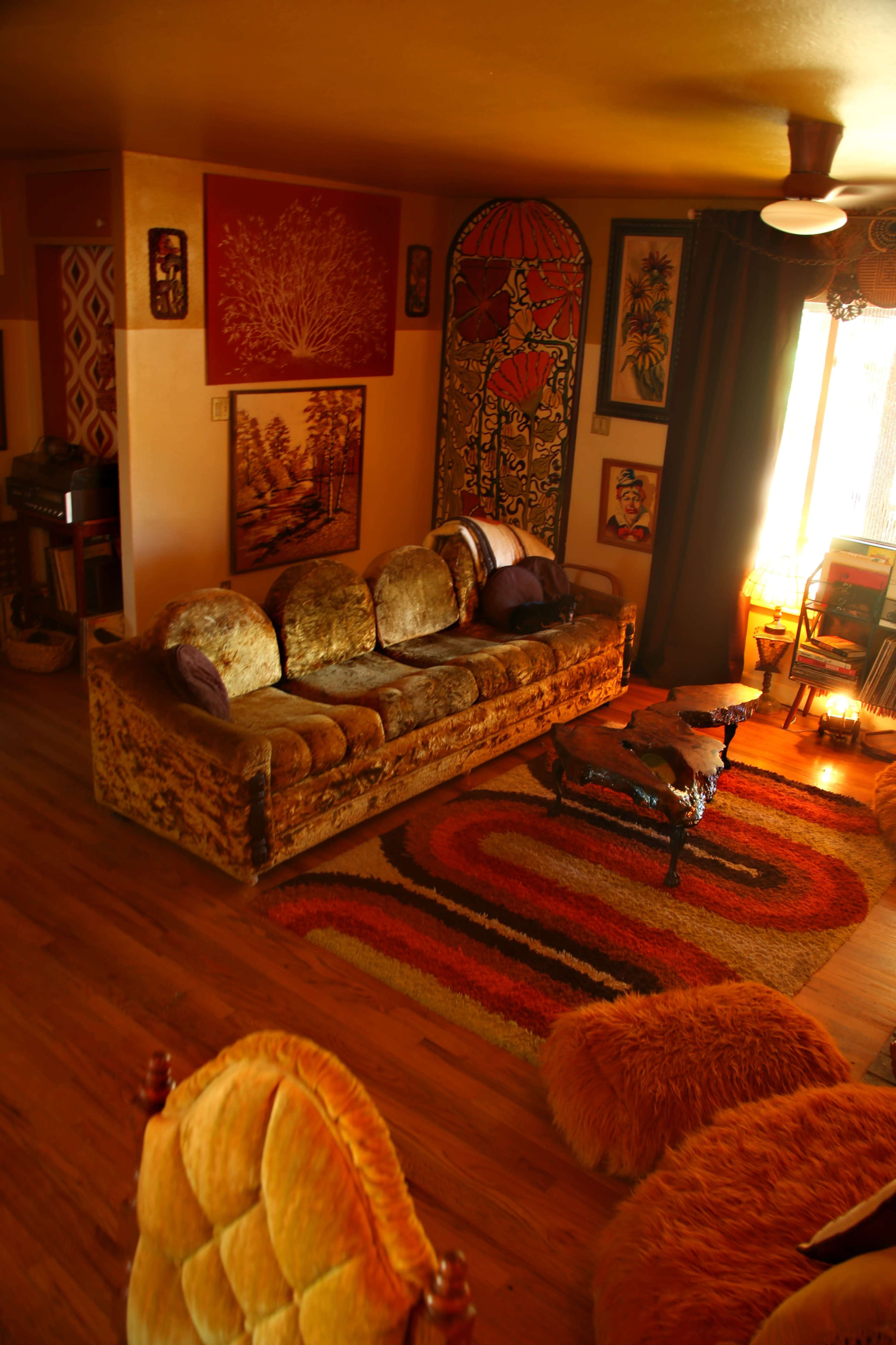 The image depicts a cozy living room with a vintage couch, colorful rugs, and several decorative artworks on the walls.