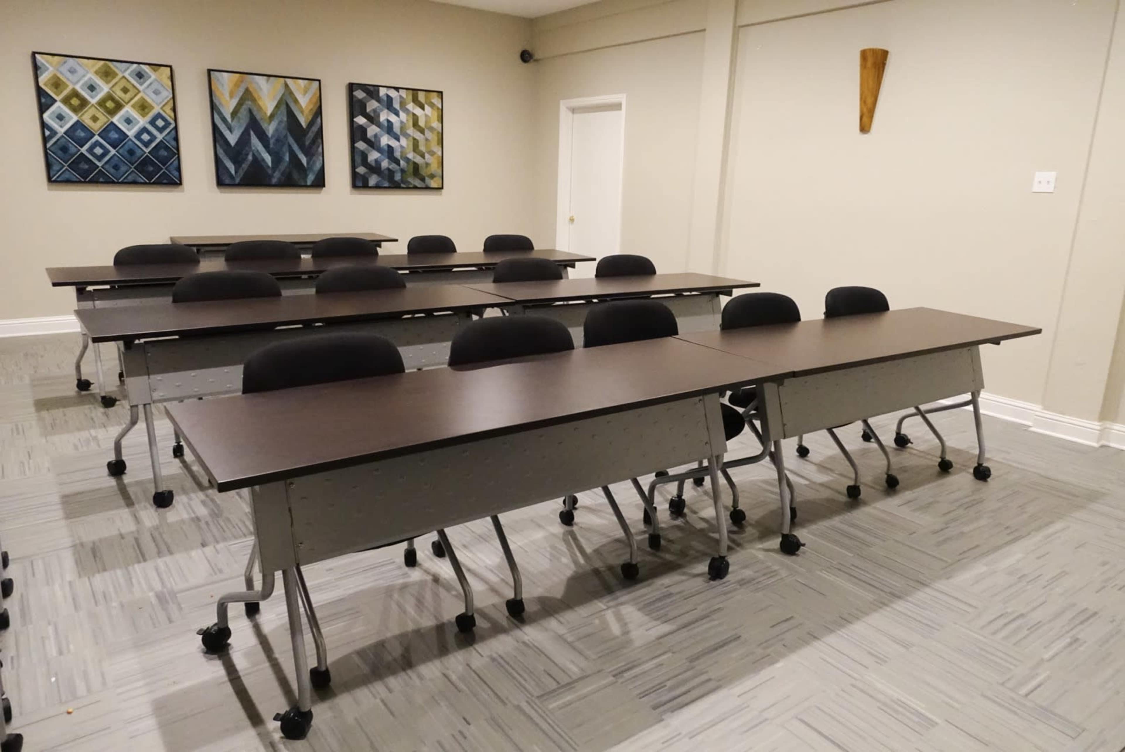 A neatly arranged meeting room features several rows of tables with rolling chairs, and abstract art on the walls.