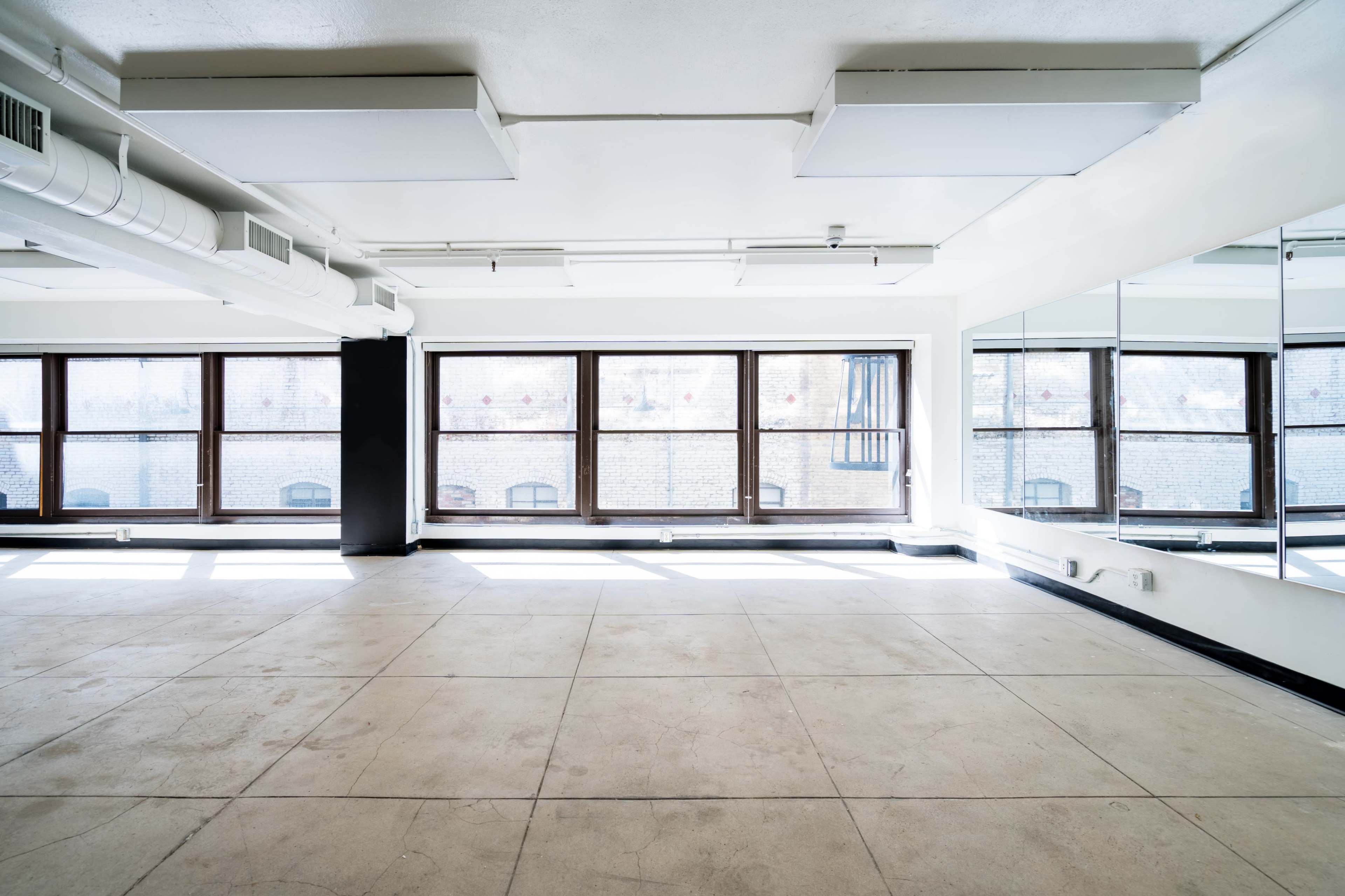 A bright, empty room features large windows and a mirrored wall.