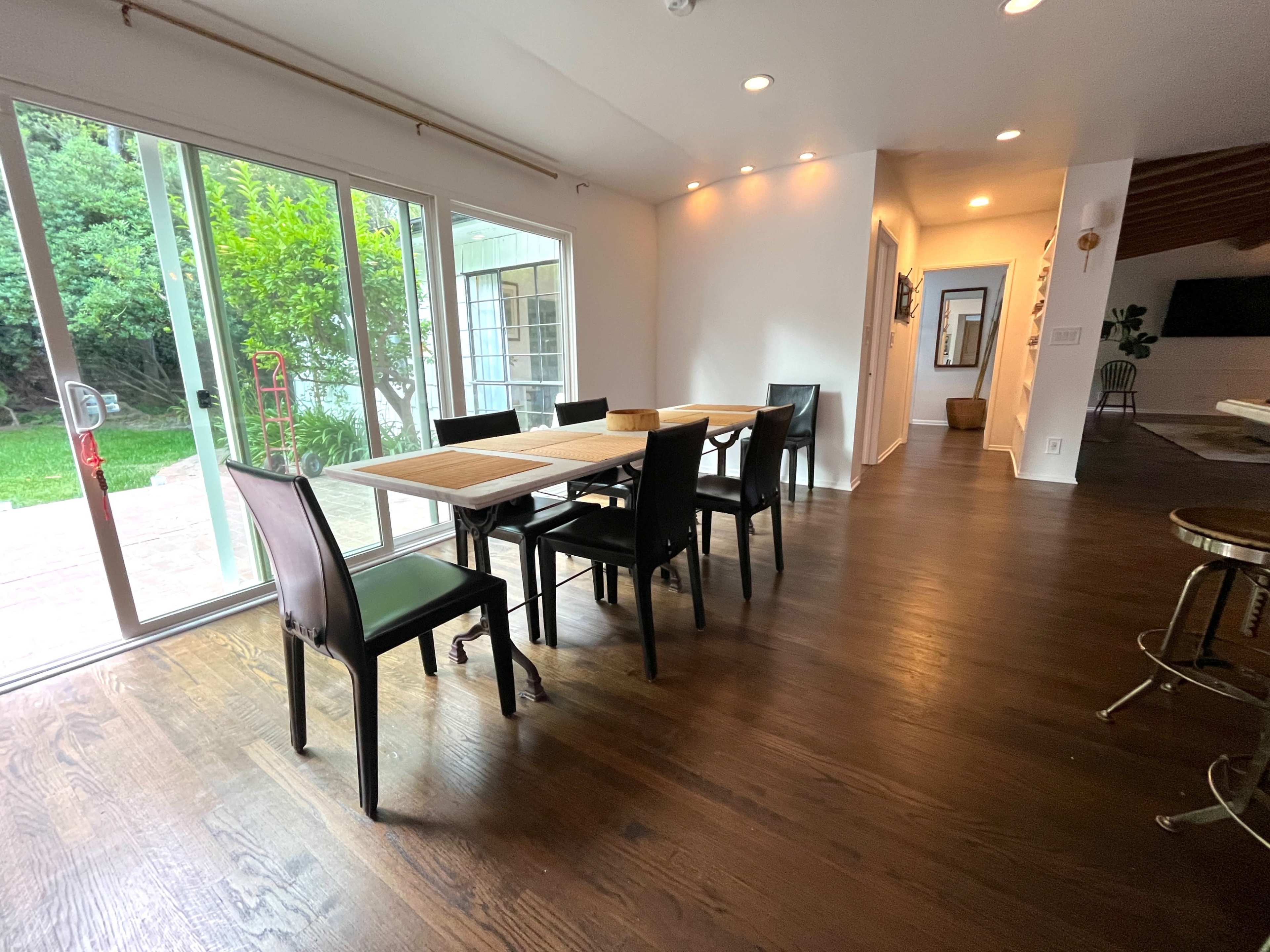 A dining area with a large wooden table surrounded by black chairs, featuring sliding glass doors that open to a green outdoor space.