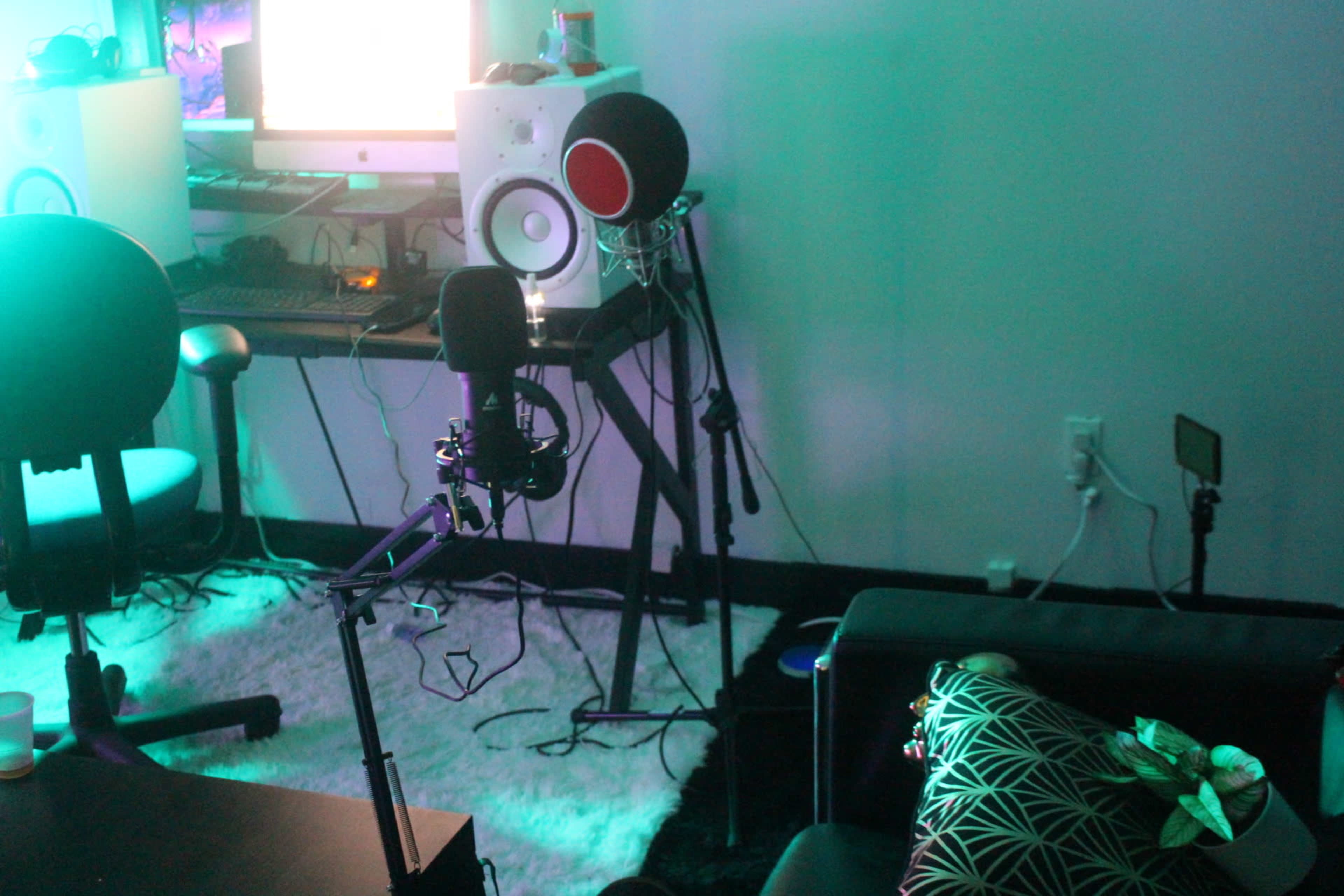 The scene features a recording setup with a microphone on a stand, computer, and audio equipment in a dimly lit room.