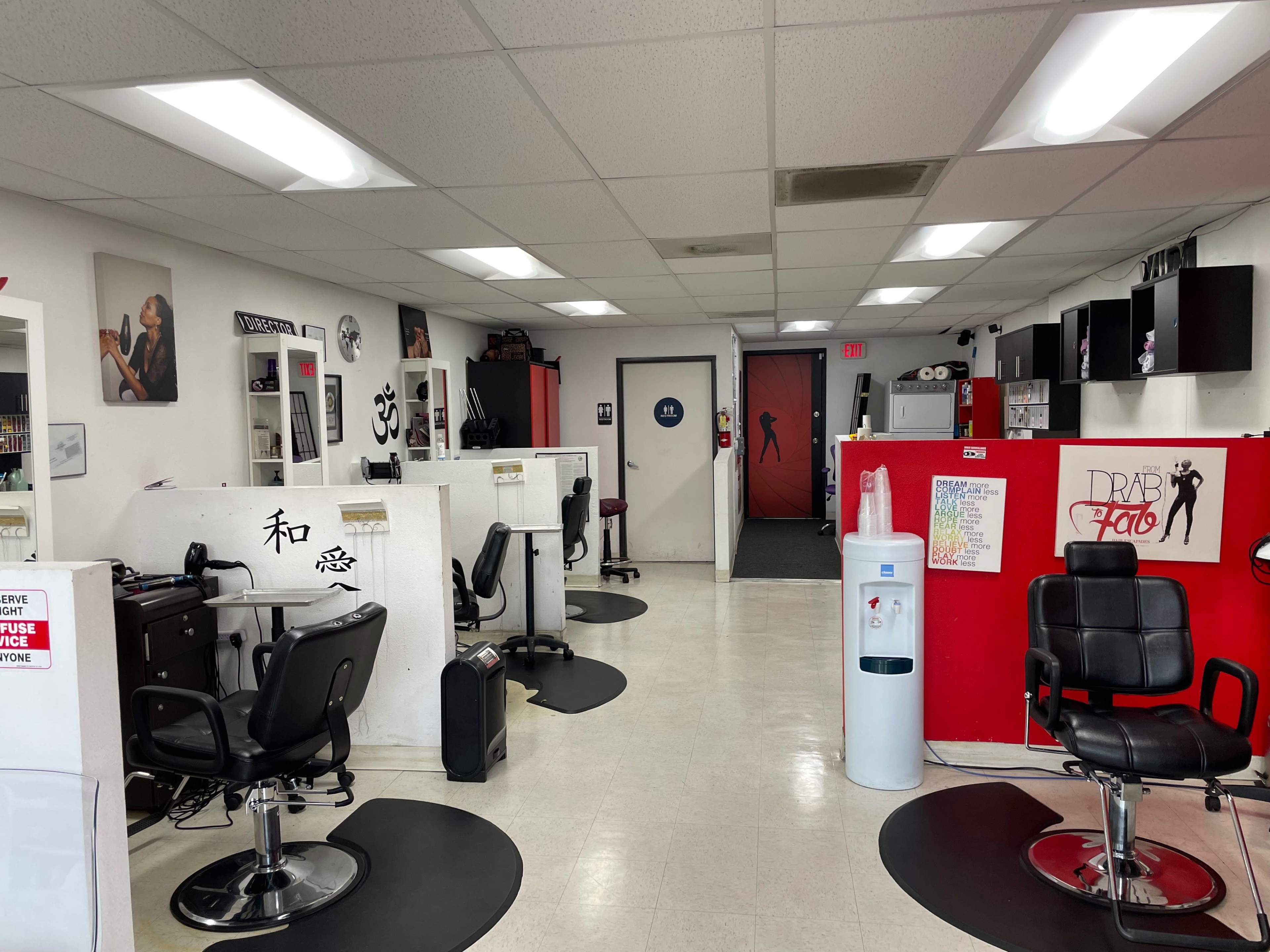 A hair salon interior with several styling stations, black swivel chairs, and a red accent wall featuring a door.