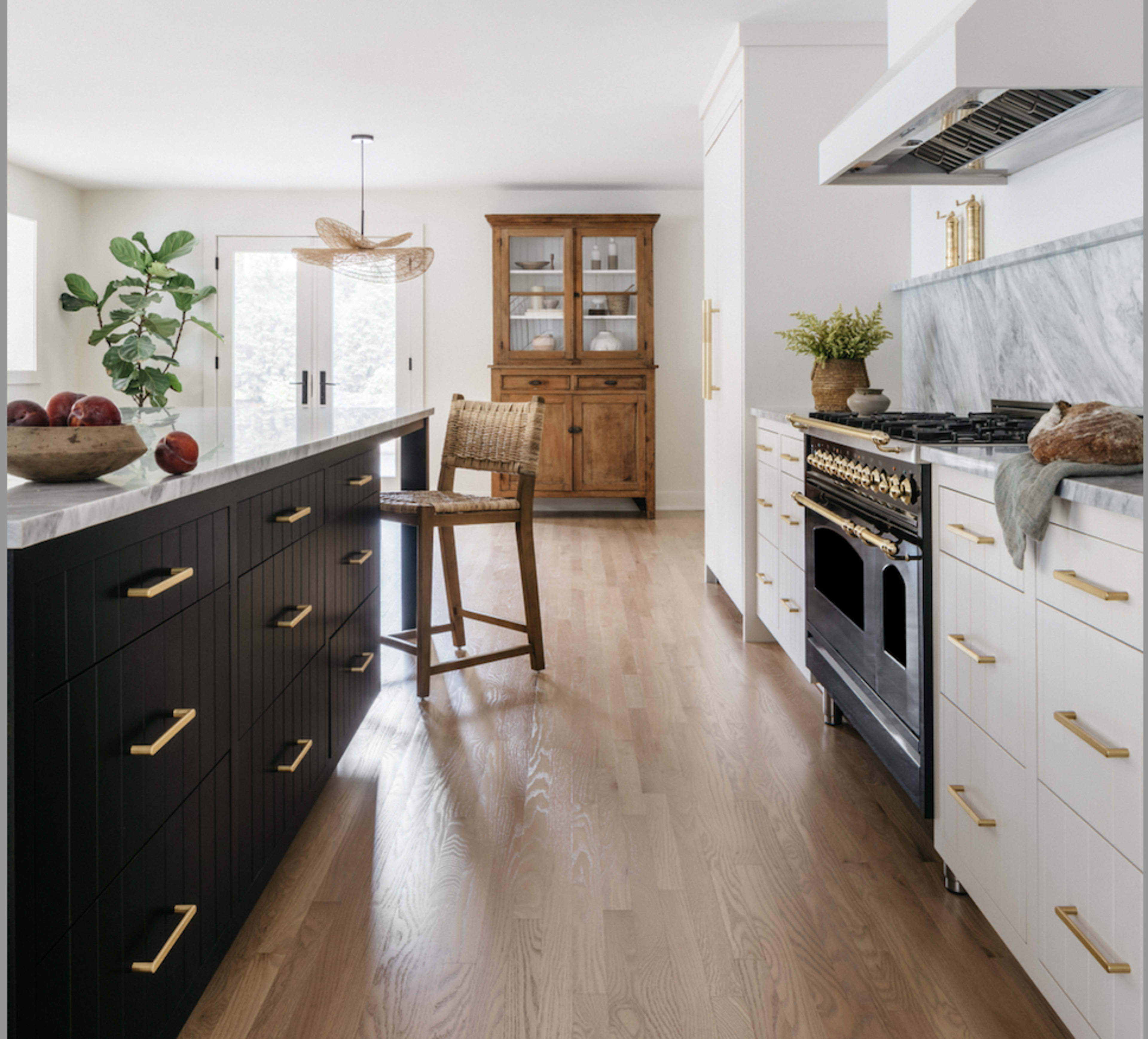 The kitchen features a central island with a black and white color scheme, a wooden dining chair, a vintage hutch, and modern appliances.