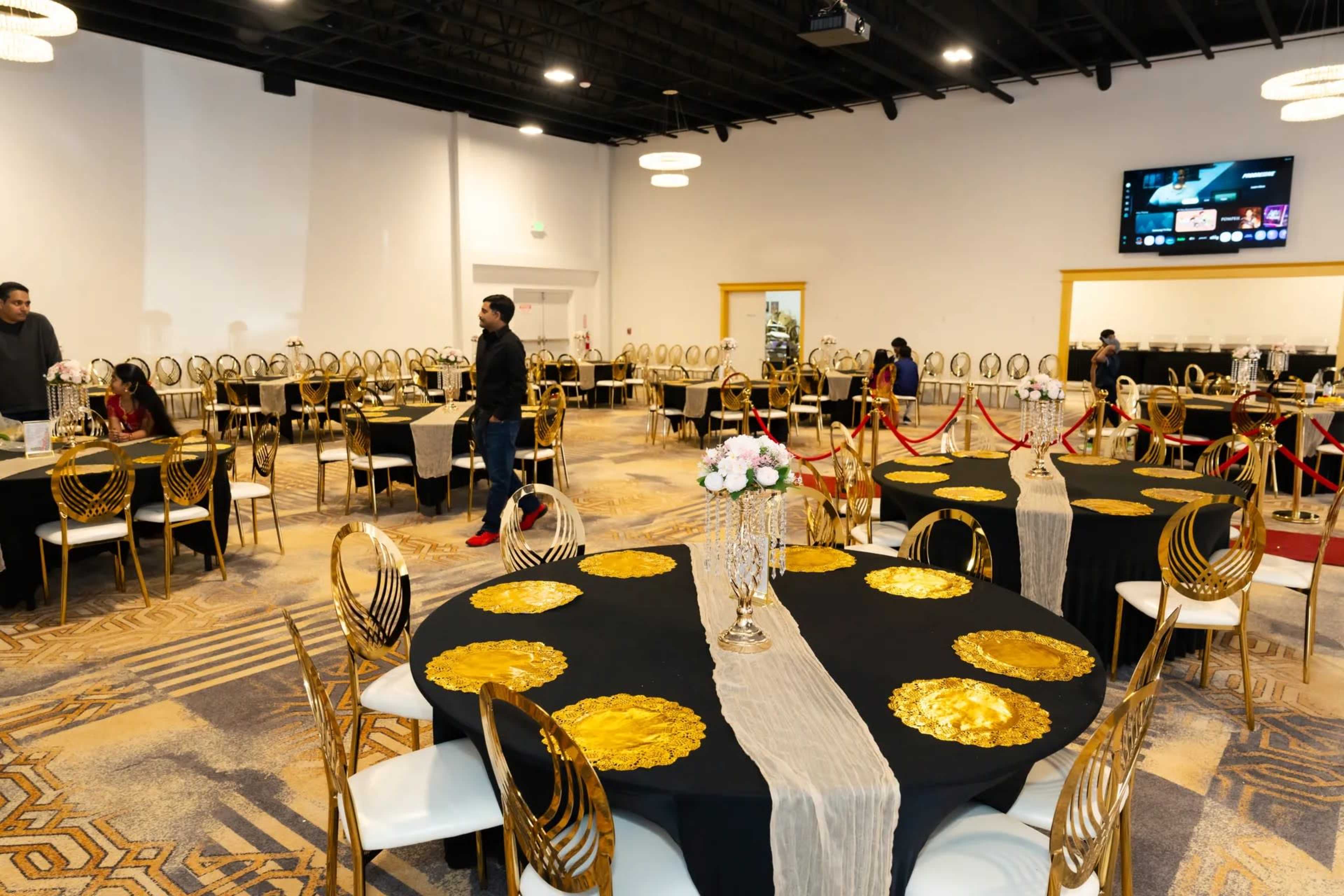 The image shows an elegant event space with round tables dressed in black cloth and gold accents, arranged in a well-organized layout.