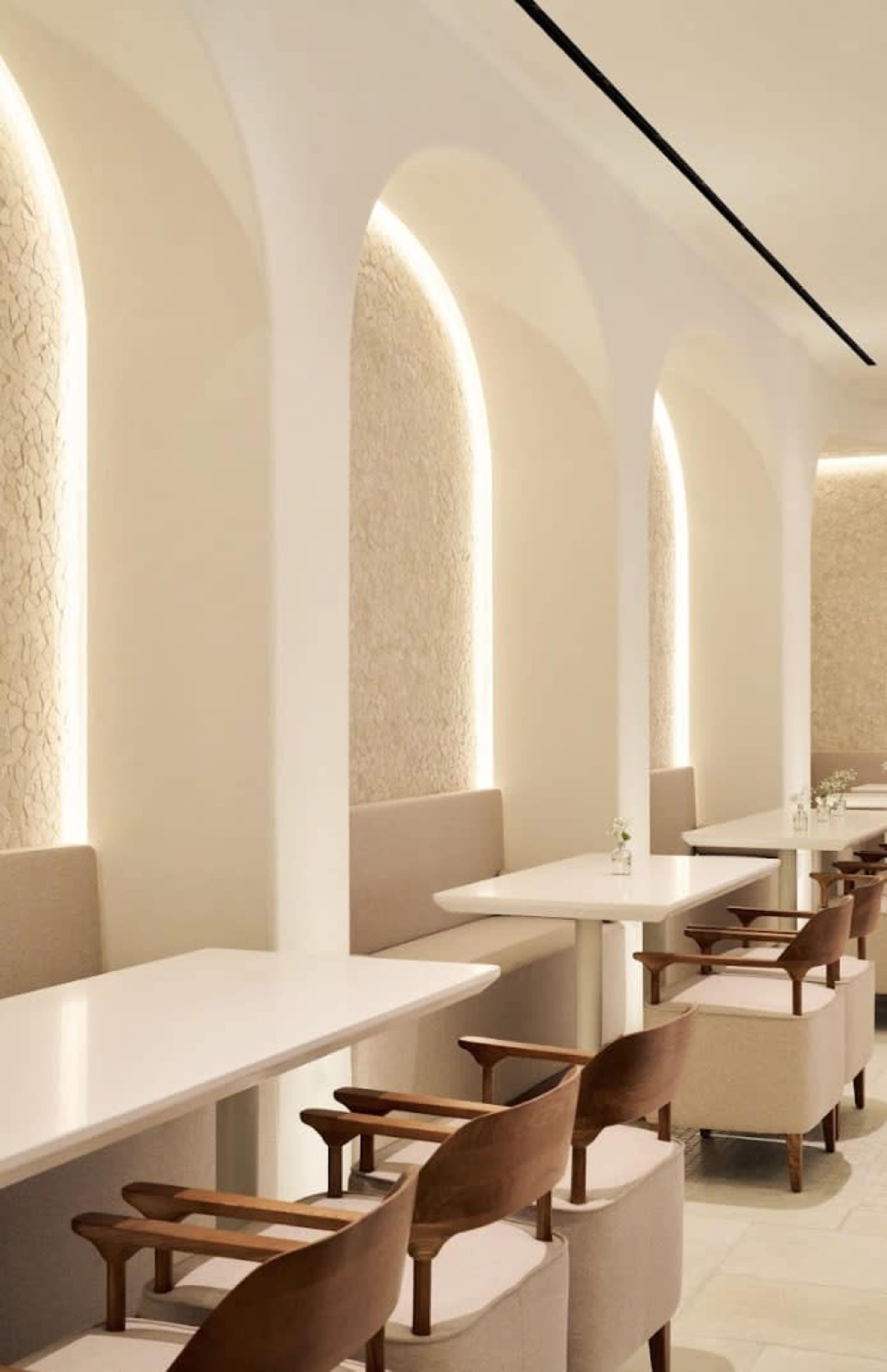 The image shows a modern café interior with light-colored walls, arched features, and wooden chairs arranged around white tables.