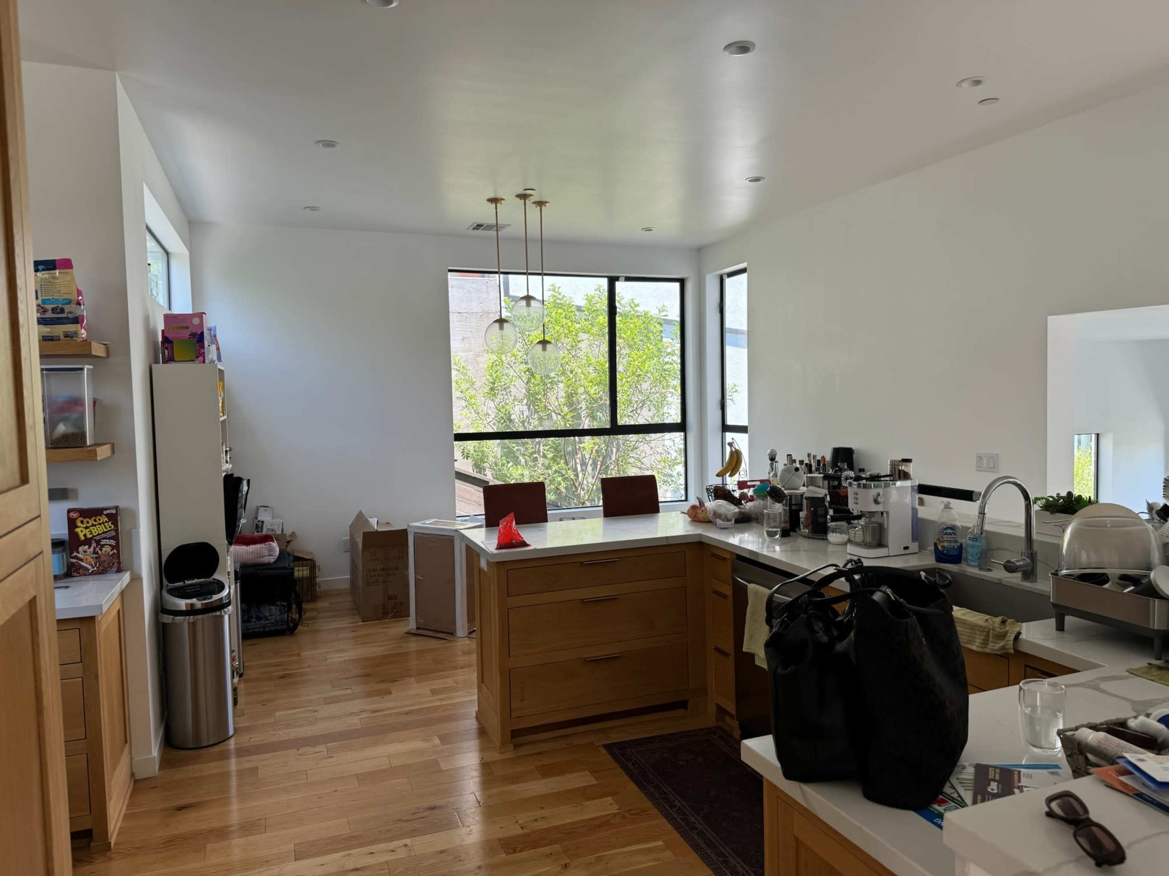 A modern kitchen features wooden cabinets, a central island, and large windows allowing natural light to enter.