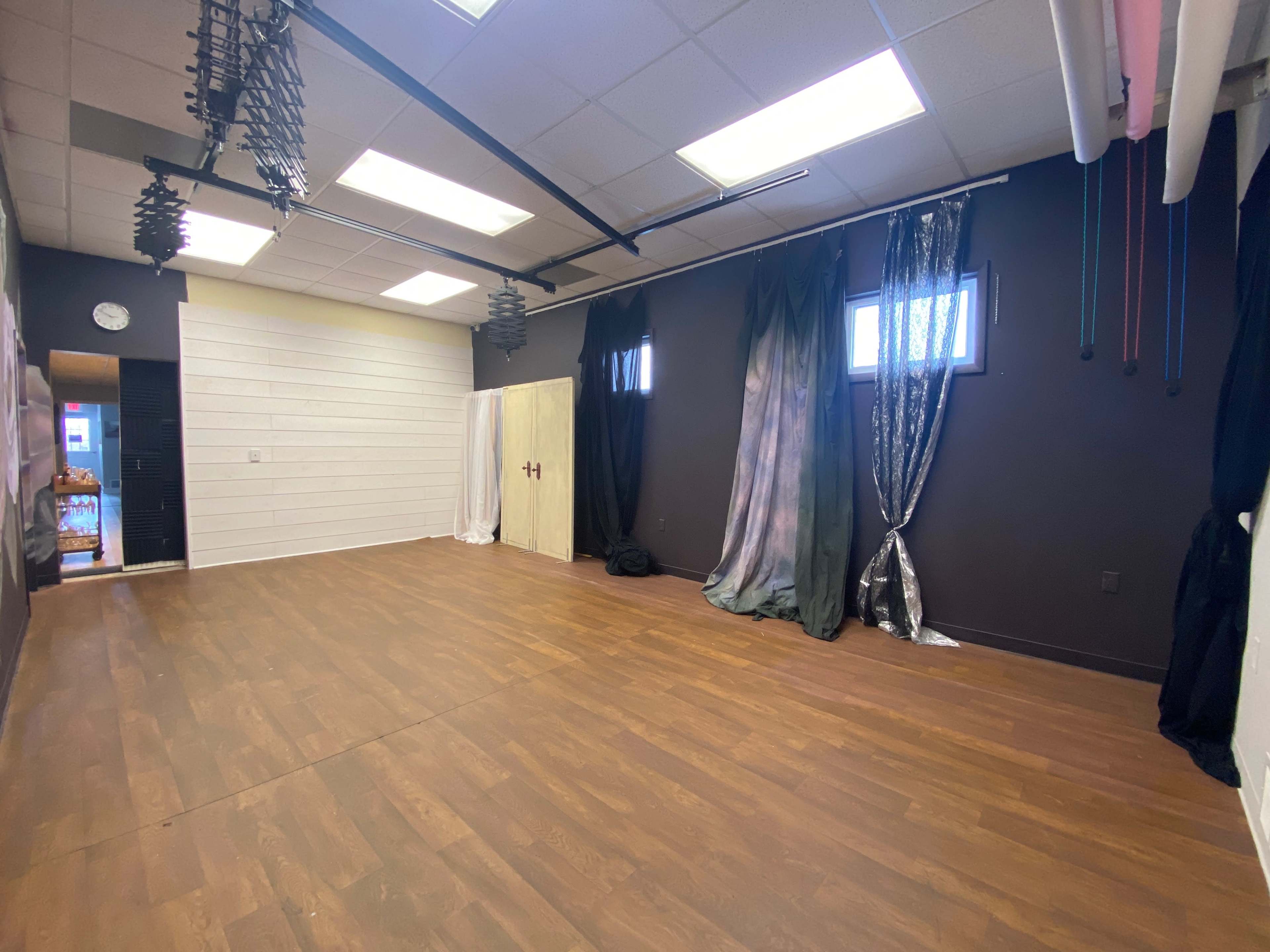 An empty room with wooden flooring, adorned with various curtains and drapes along one wall, and a clock on the opposite wall.
