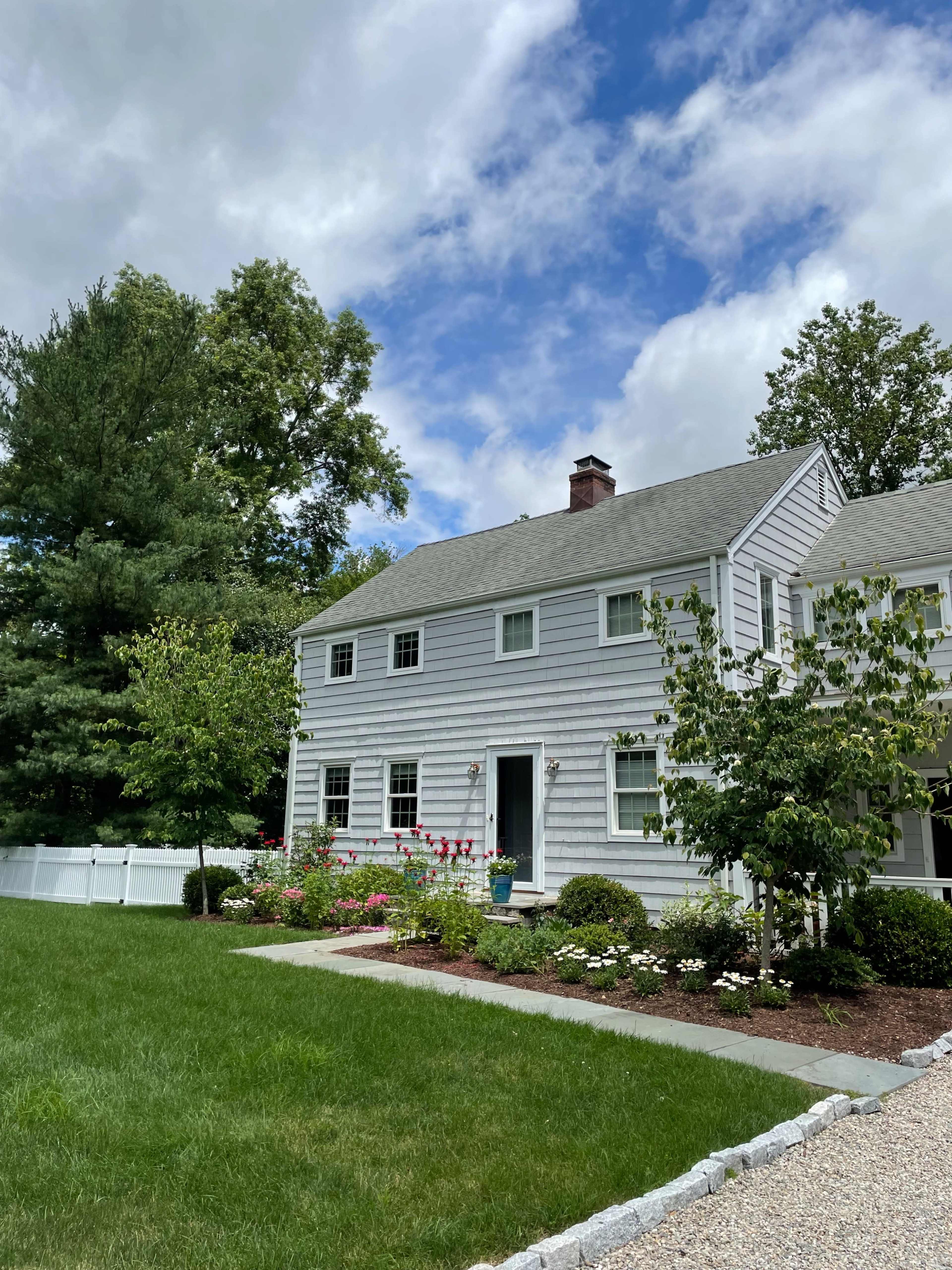 A well-maintained two-story house with gray siding and a manicured lawn features flower beds and a gravel pathway.
